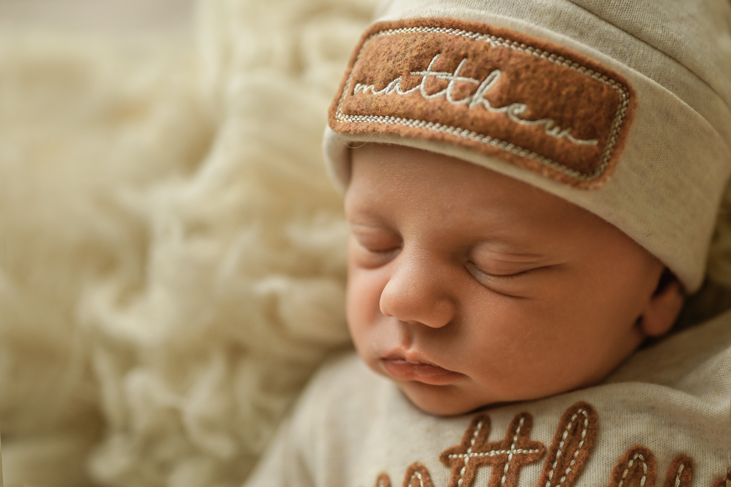 Sleeping newborn baby named Matthew wearing a personalized beige knit hat with name patch.