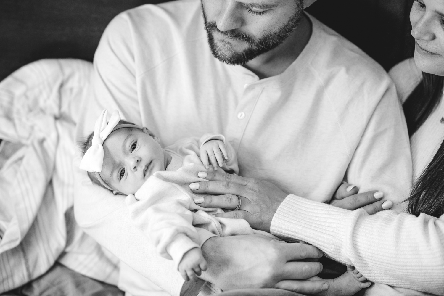 Black and white photo of parents cradling their newborn baby, sharing a tender family moment together.