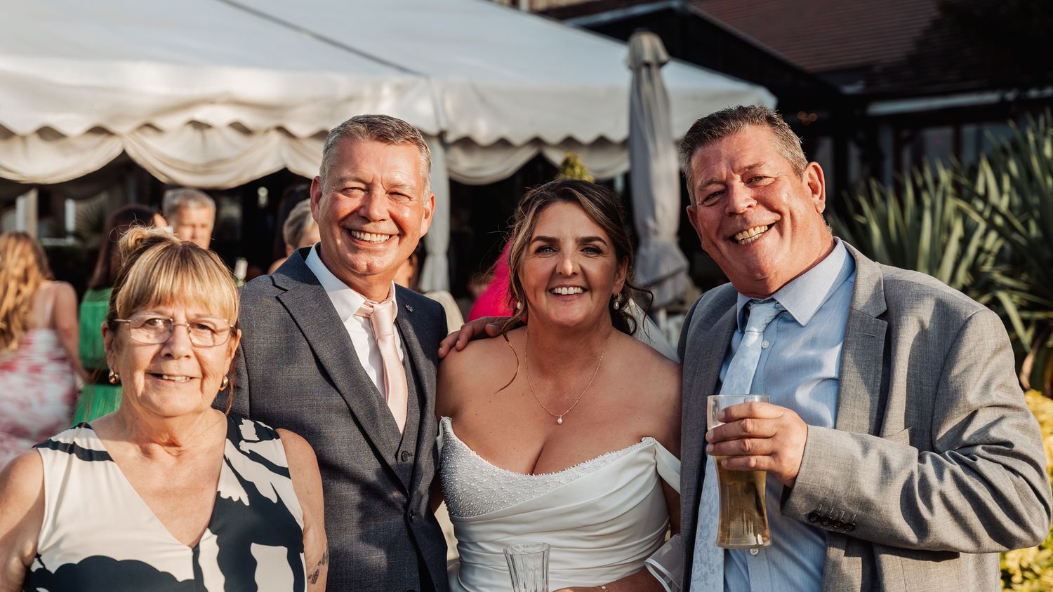 Bride poses with three smiling family members at outdoor wedding reception celebration.