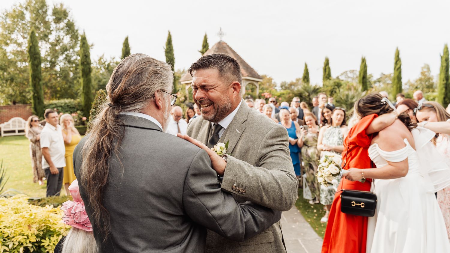 Groom shares joyful handshake with guest during outdoor wedding ceremony celebration.