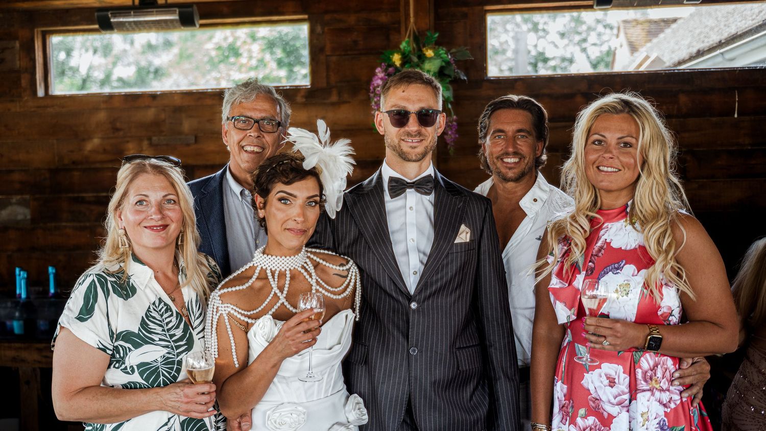 Group of six people posing together at a wedding celebration inside a rustic wooden venue.