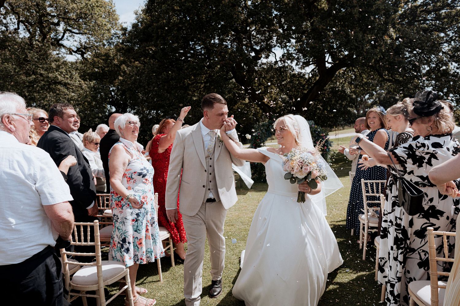 Bride and groom walk back down the aisle after outdoor wedding ceremony surrounded by cheering guests.