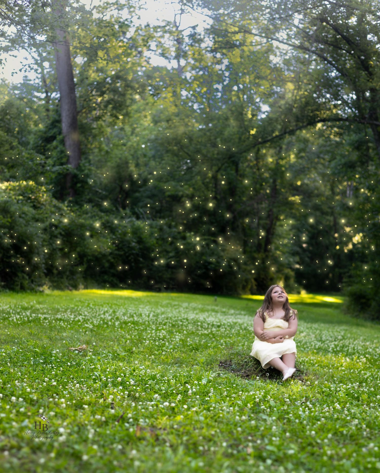 A young girl in a yellow dress sits on grass surrounded by magical glowing fireflies in a green park.