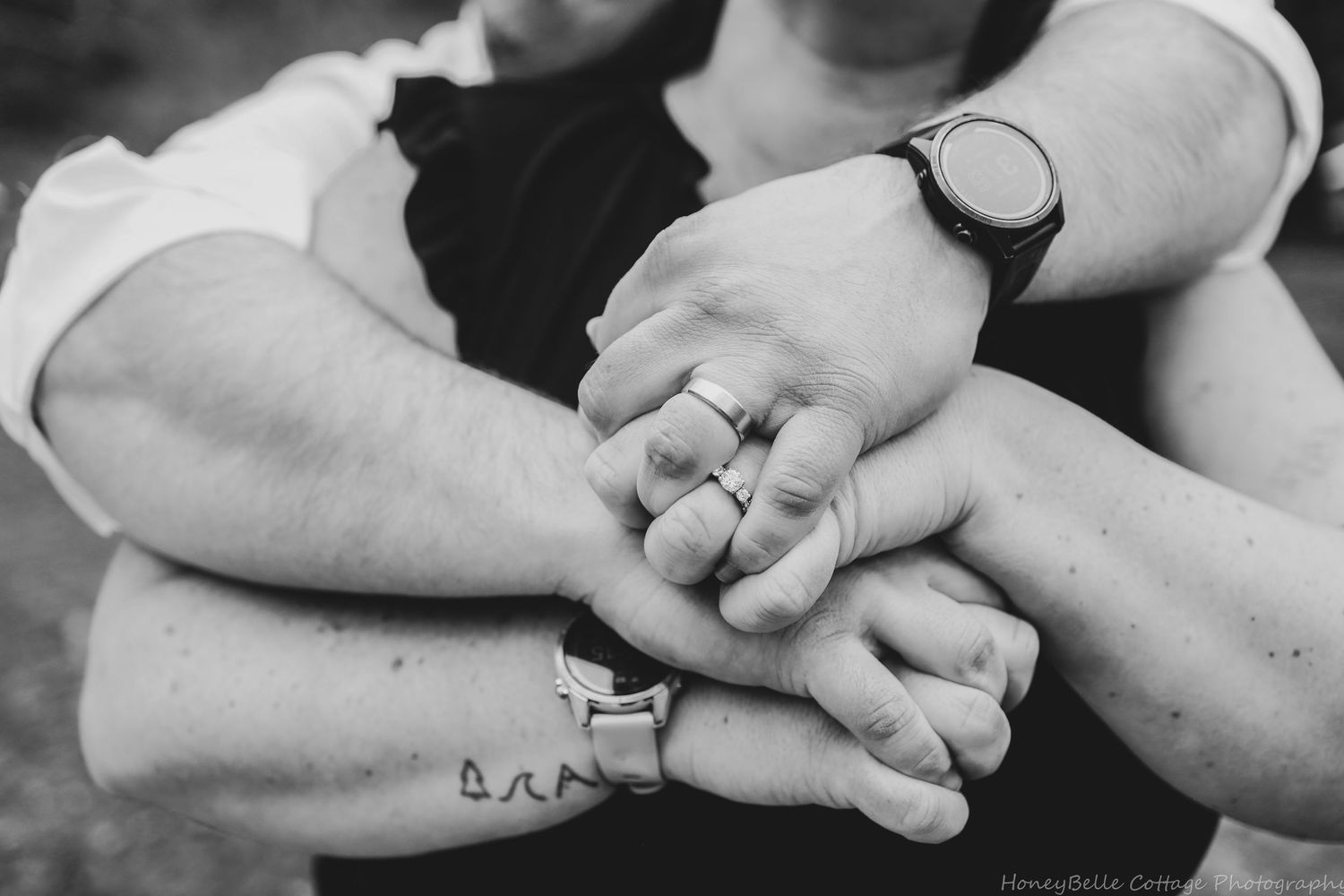 Black and white photo of two people holding hands together, showing wedding rings and a watch, symbolizing love and commitment.