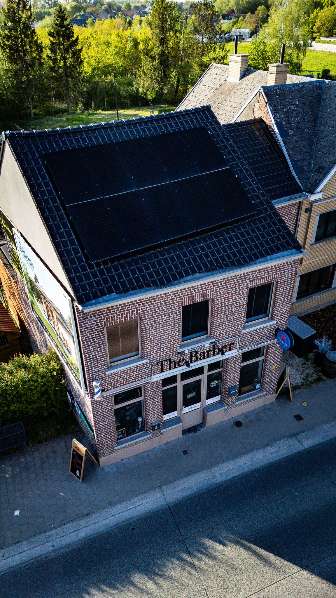 Aerial view of a brick barbershop building with solar panels on the roof, located on a street corner.