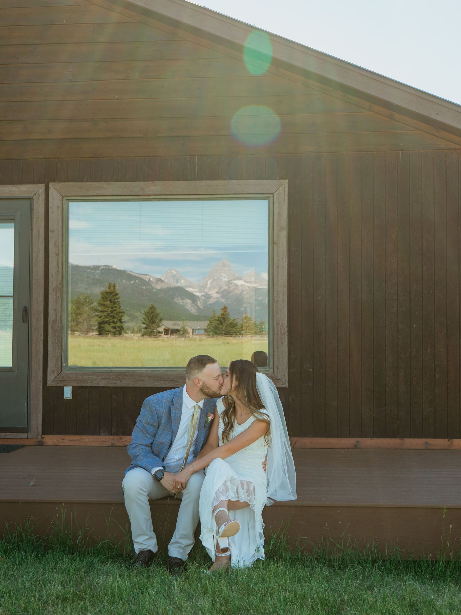Bride and groom share a kiss on cabin steps with a stunning mountain backdrop on their wedding day.