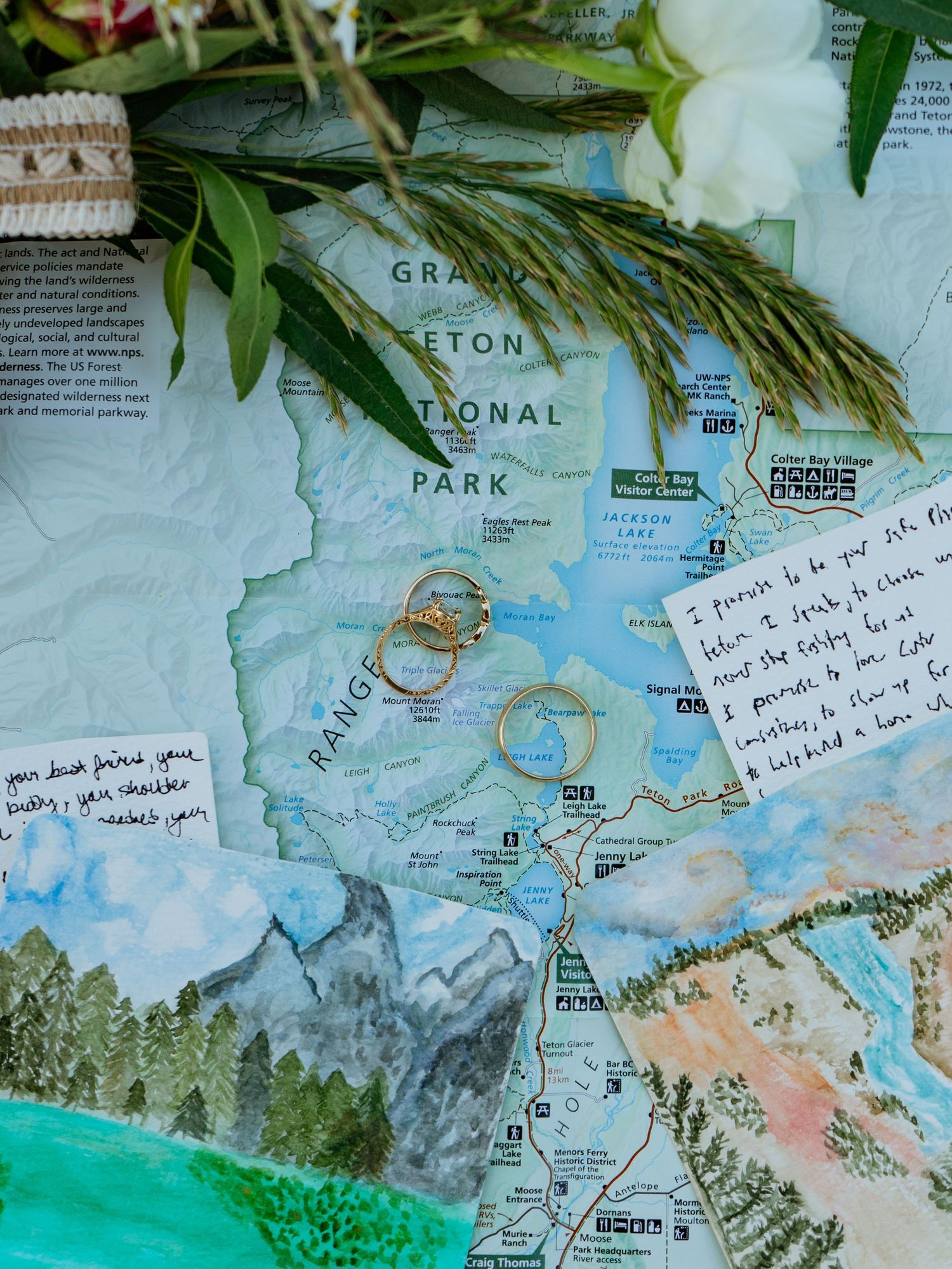 Wedding rings resting on a Grand Teton National Park map with handwritten vows, flowers, and greenery.