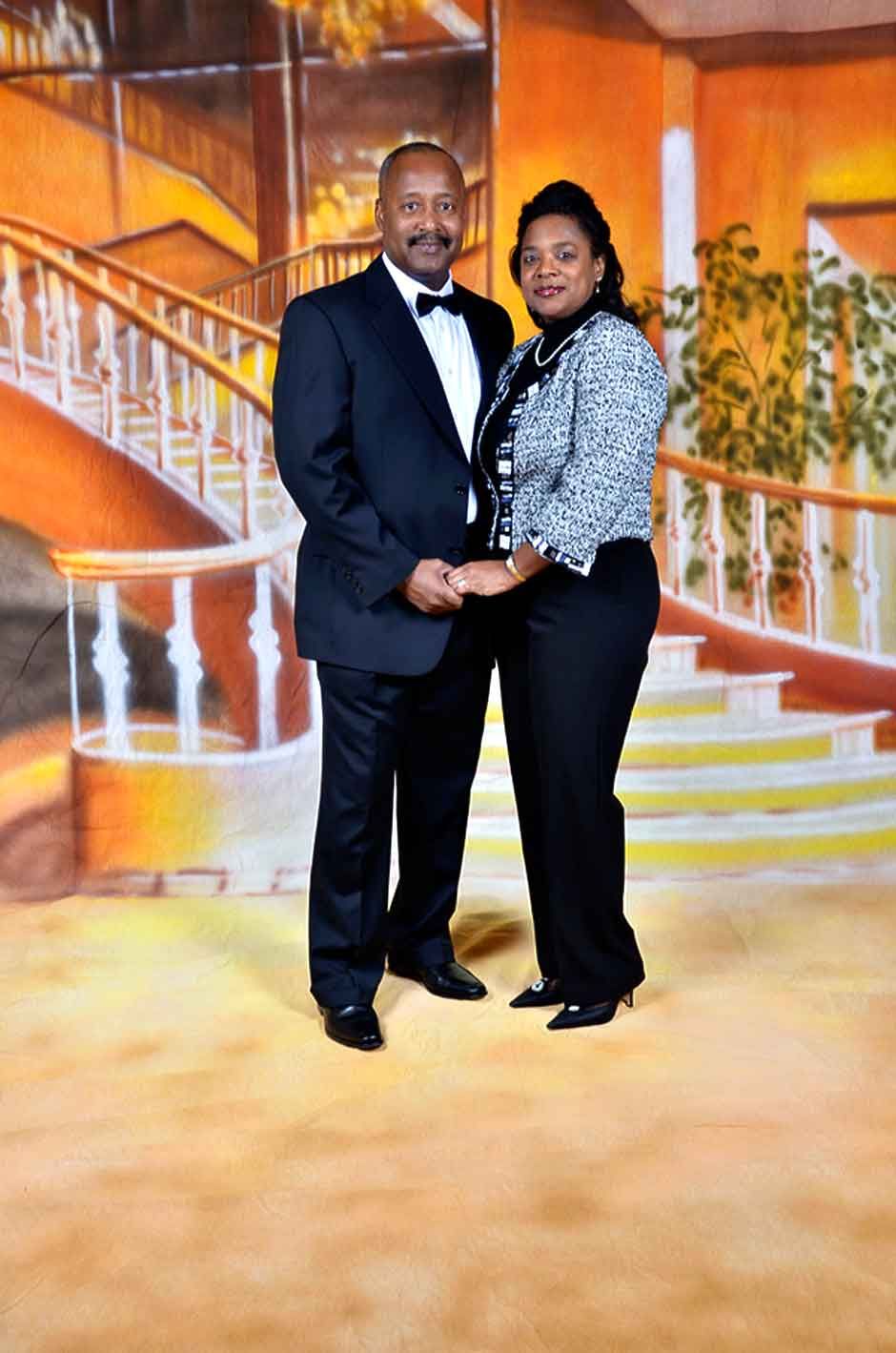 Elegant couple posing together in formal attire in front of a painted staircase backdrop.