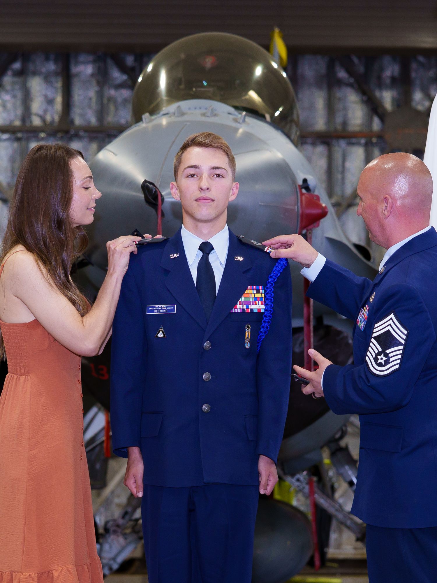 Young Air Force airman receives rank insignia pinned by family member and senior officer in front of military jet.