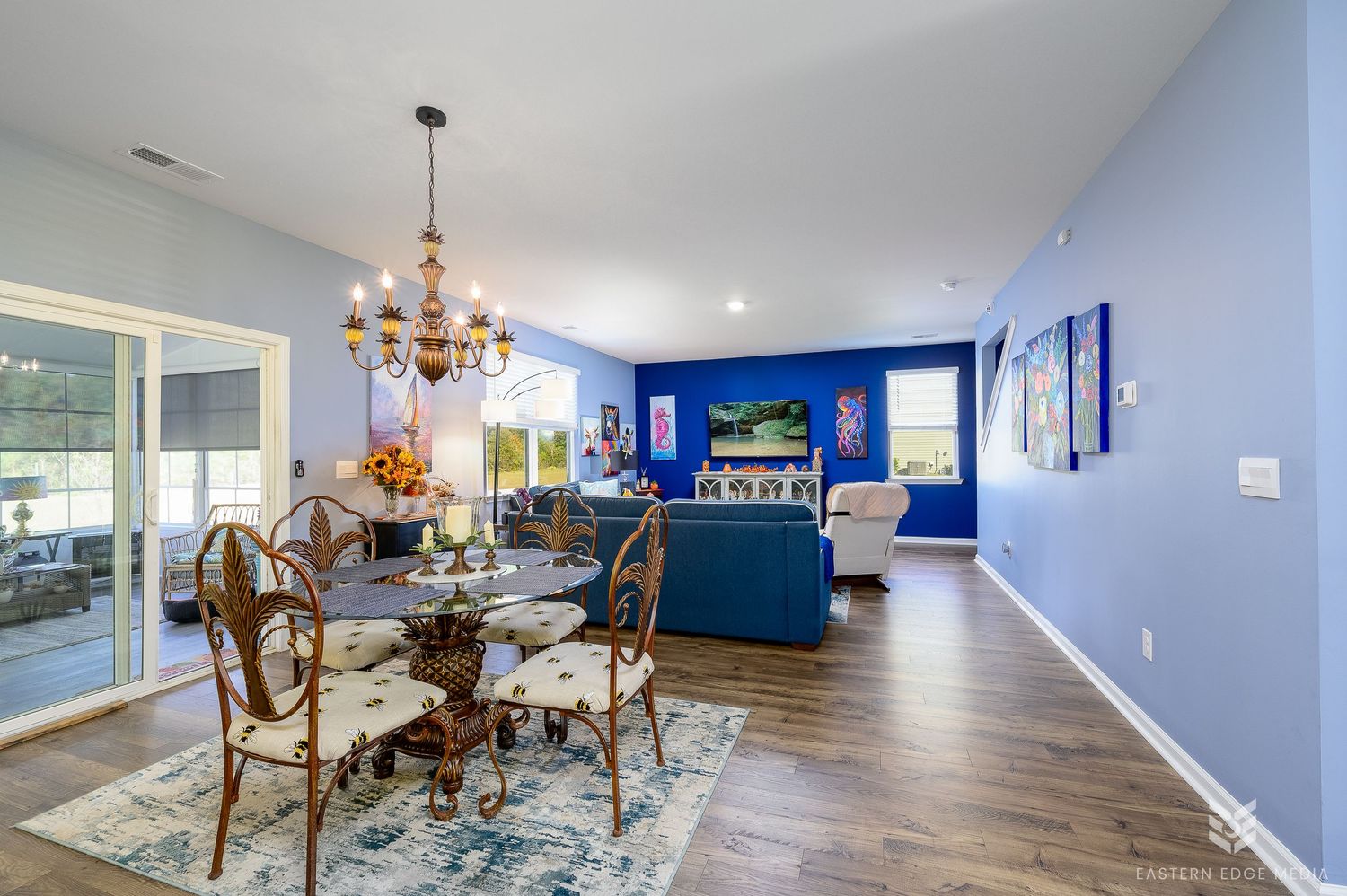 Bright blue dining and living room with chandelier and hardwood floors.