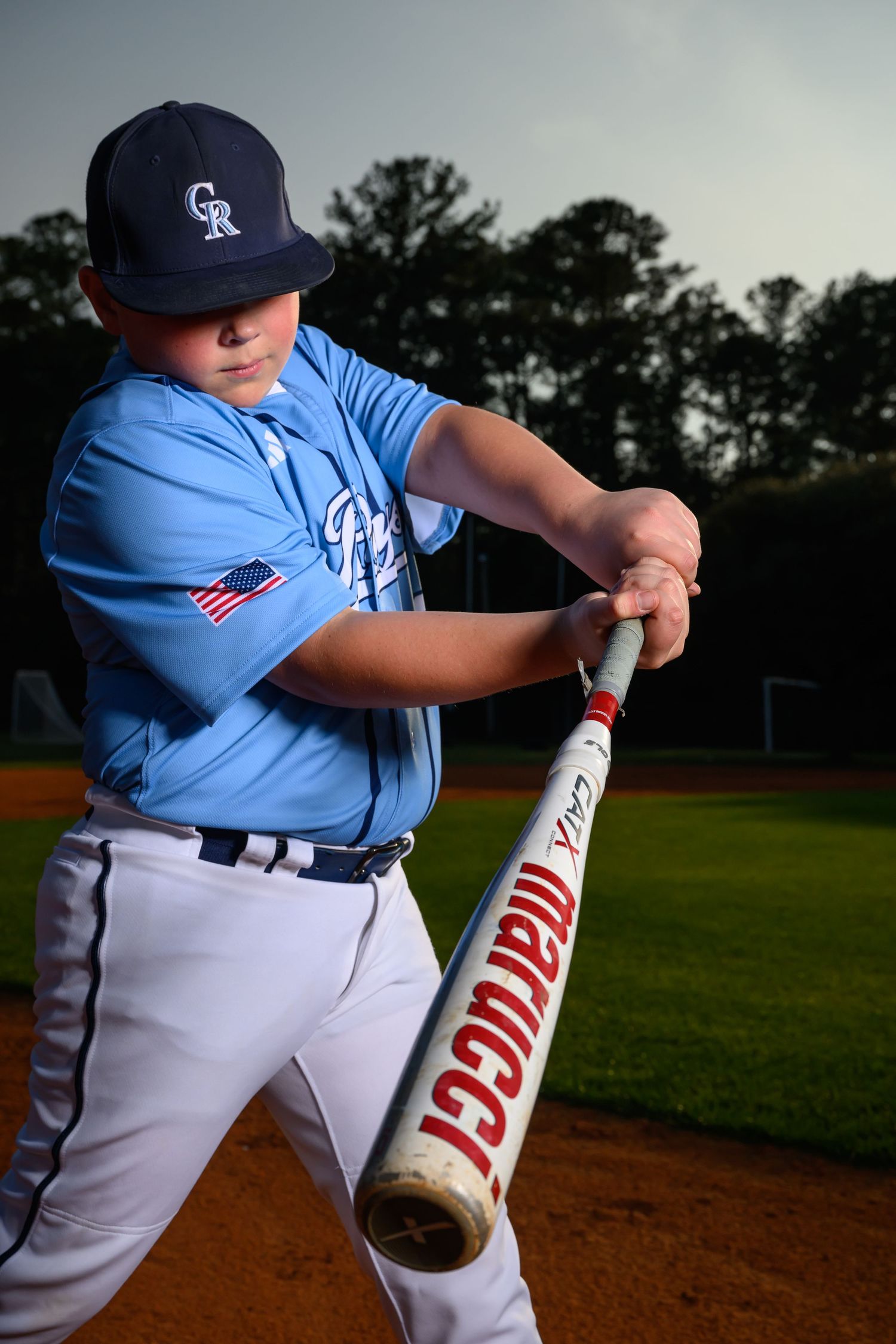 Youth baseball player in blue uniform practices batting stance with Marucci bat on field.