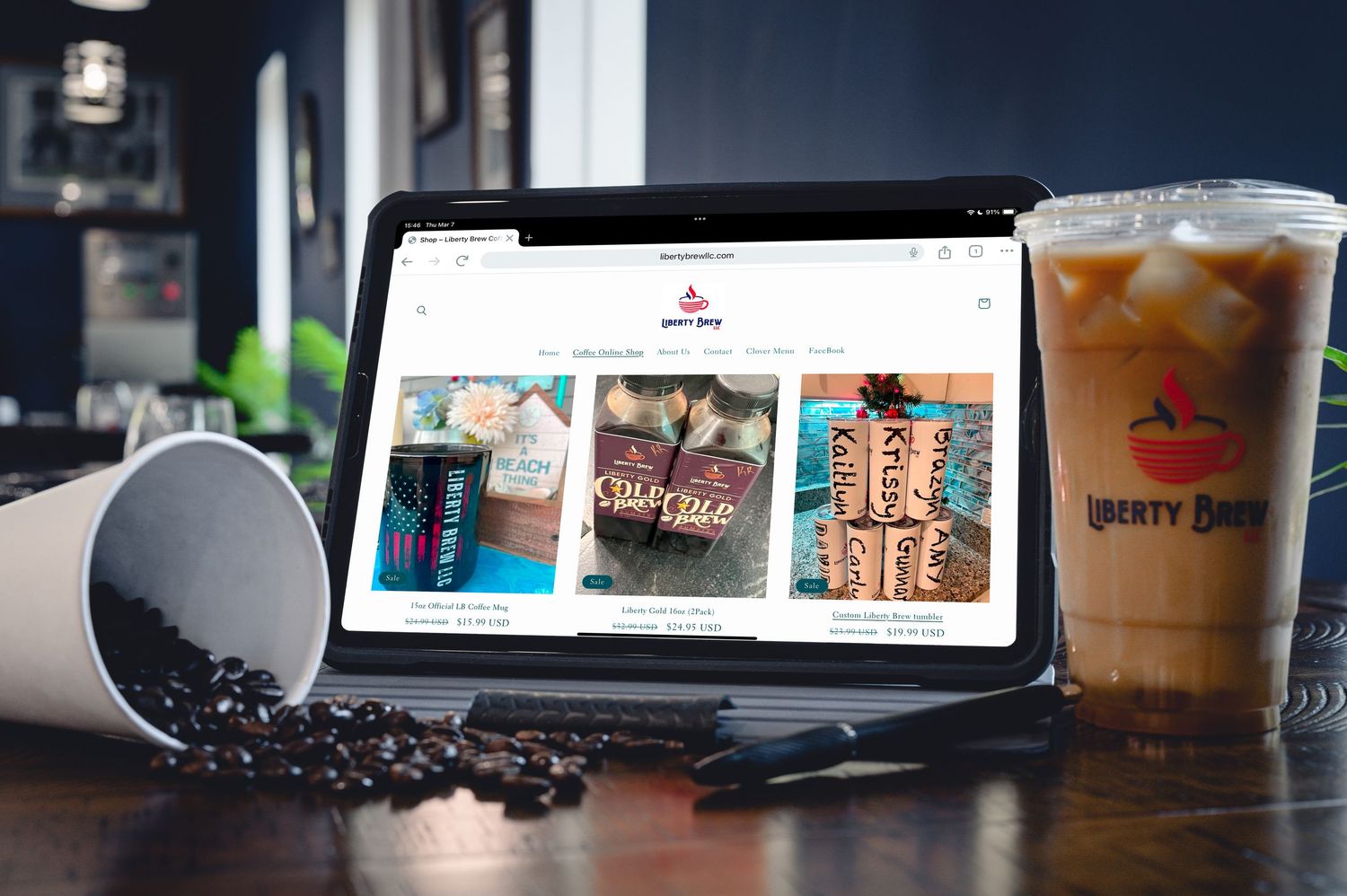 Liberty Brew coffee shop website displayed on laptop with iced coffee nearby.