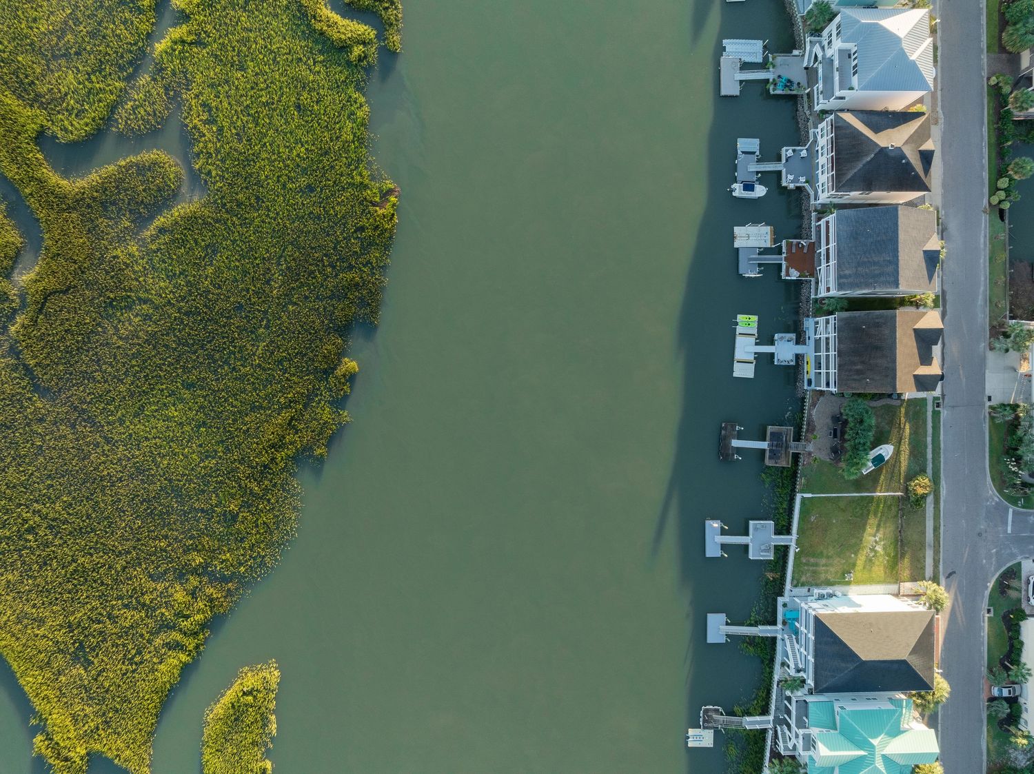 Aerial top-down view of waterfront homes with private docks along a green marsh-lined canal.