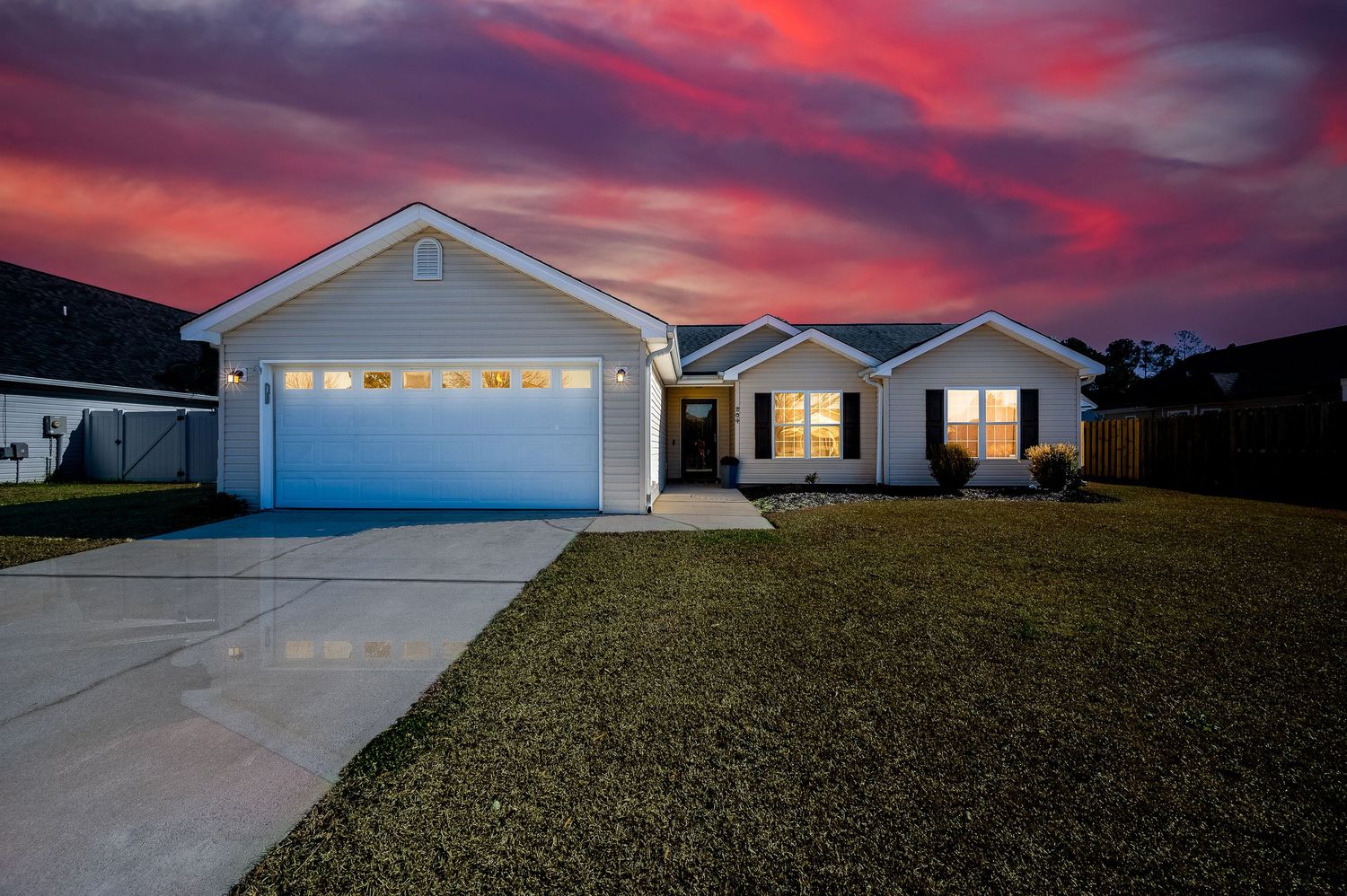 Single-story ranch home with two-car garage and lush lawn at vibrant sunset.