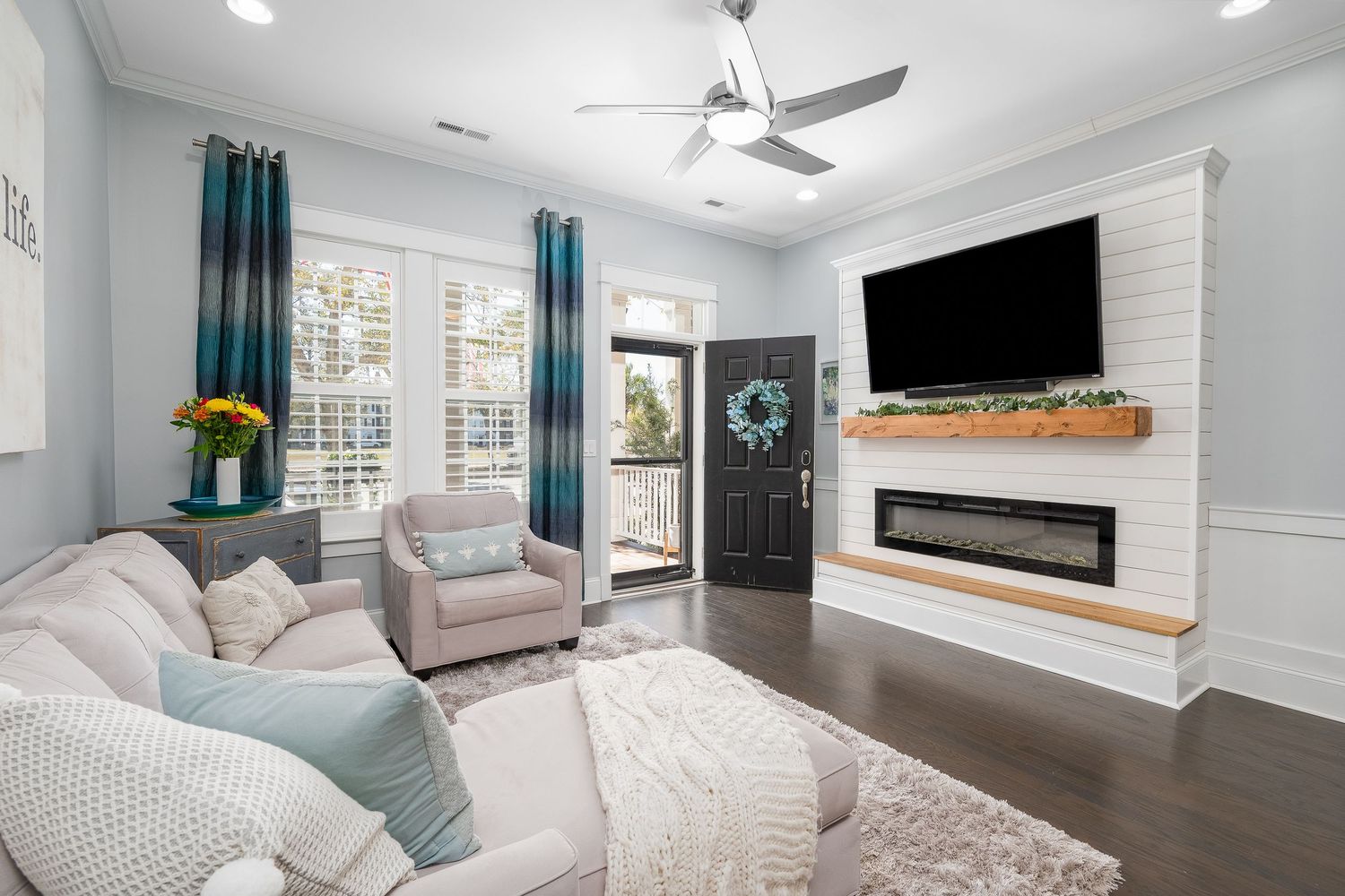 Contemporary living room with shiplap fireplace, wall-mounted TV, ceiling fan, and dark hardwood floors.