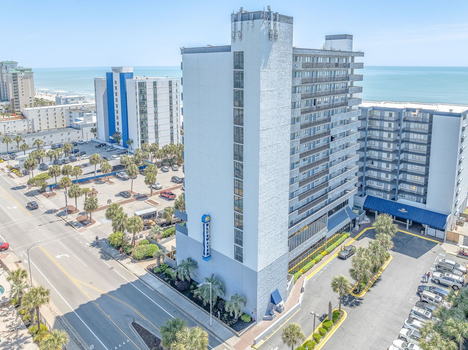 Aerial view of Bluewater Resort tower with ocean backdrop and street-level parking in Myrtle Beach.