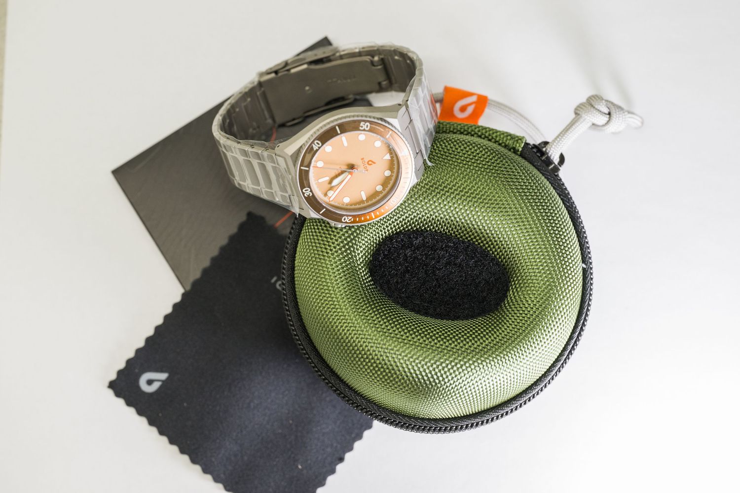 Watch with bronze dial displayed on green case with cleaning cloth and box.