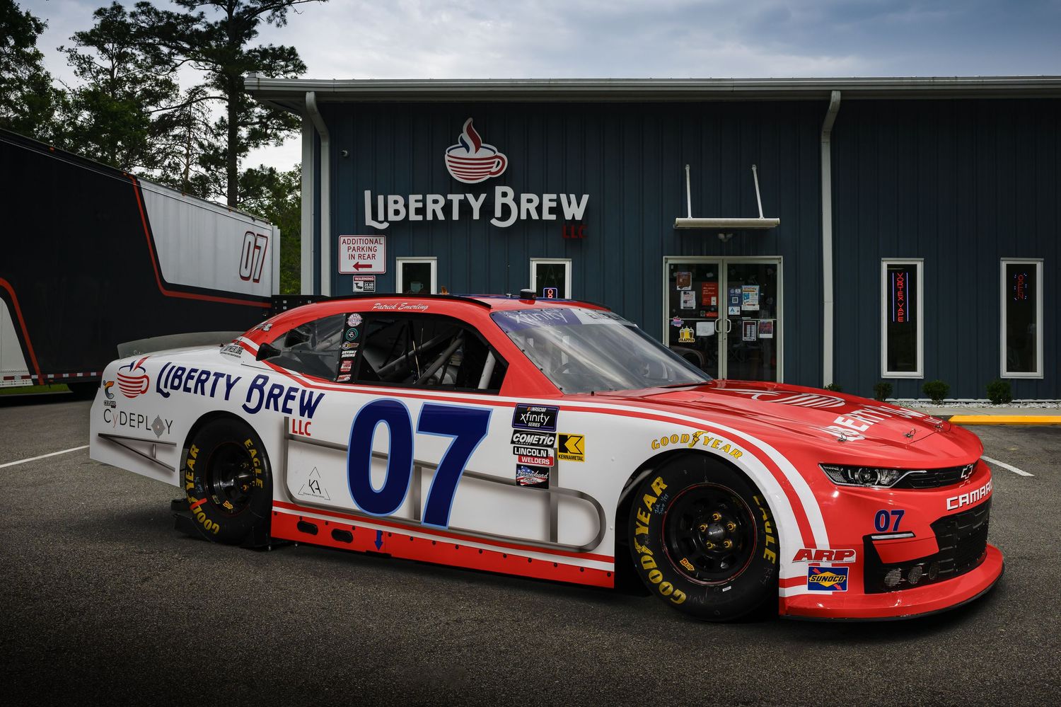 Red and white NASCAR race car with Liberty Brew sponsorship parked outside brewery.
