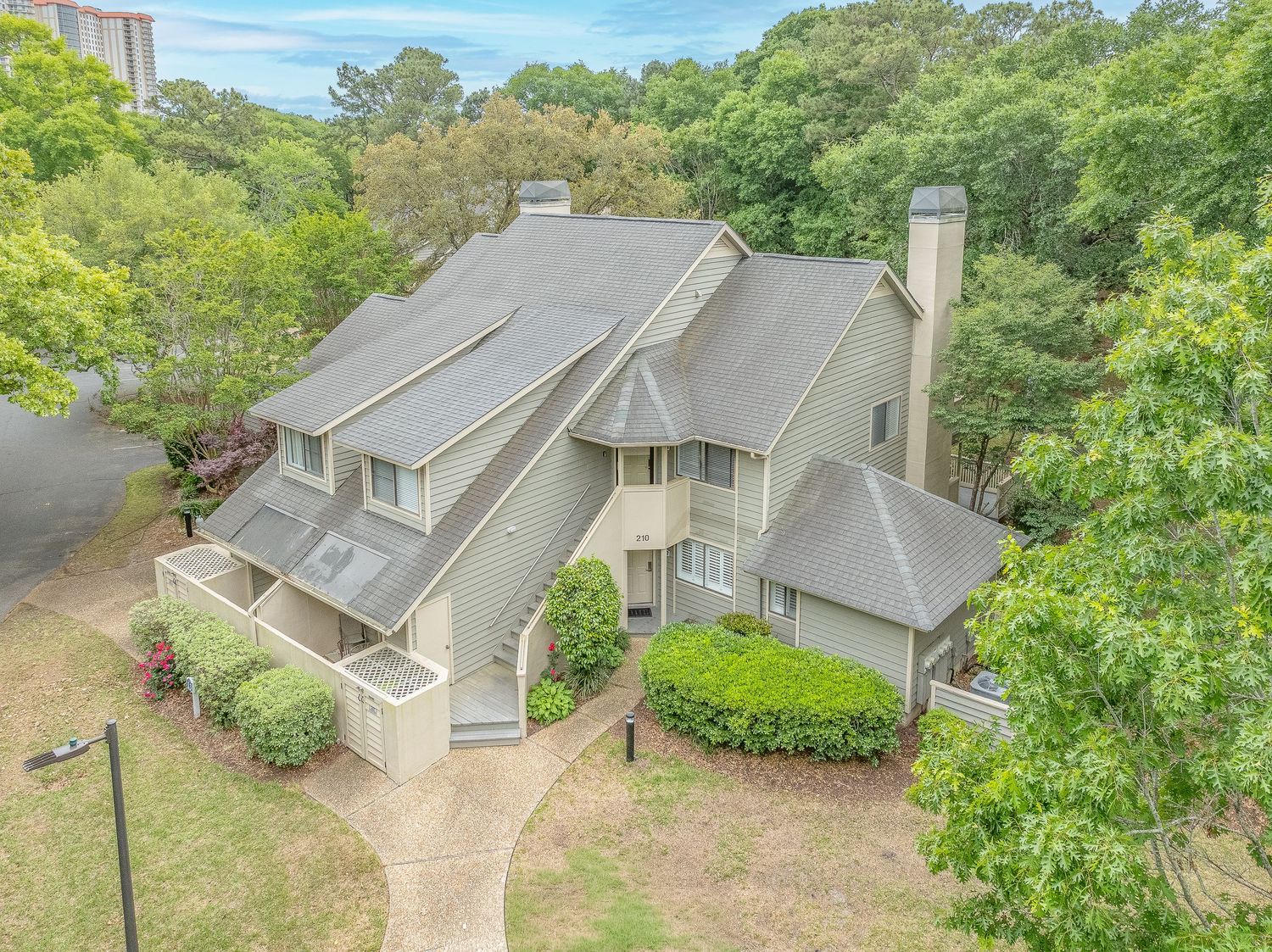 Aerial view of multi-story brown wood-sided home surrounded by mature trees near coast.