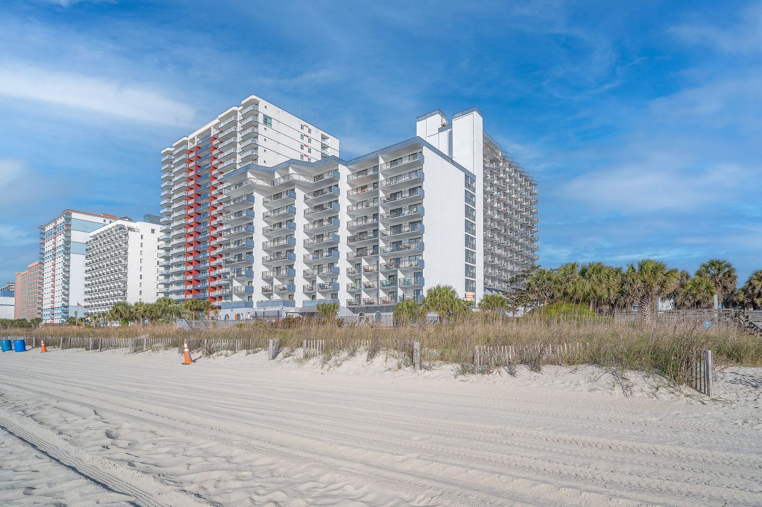 Beachfront high-rise condominiums viewed from sandy shore with dunes and clear blue sky.