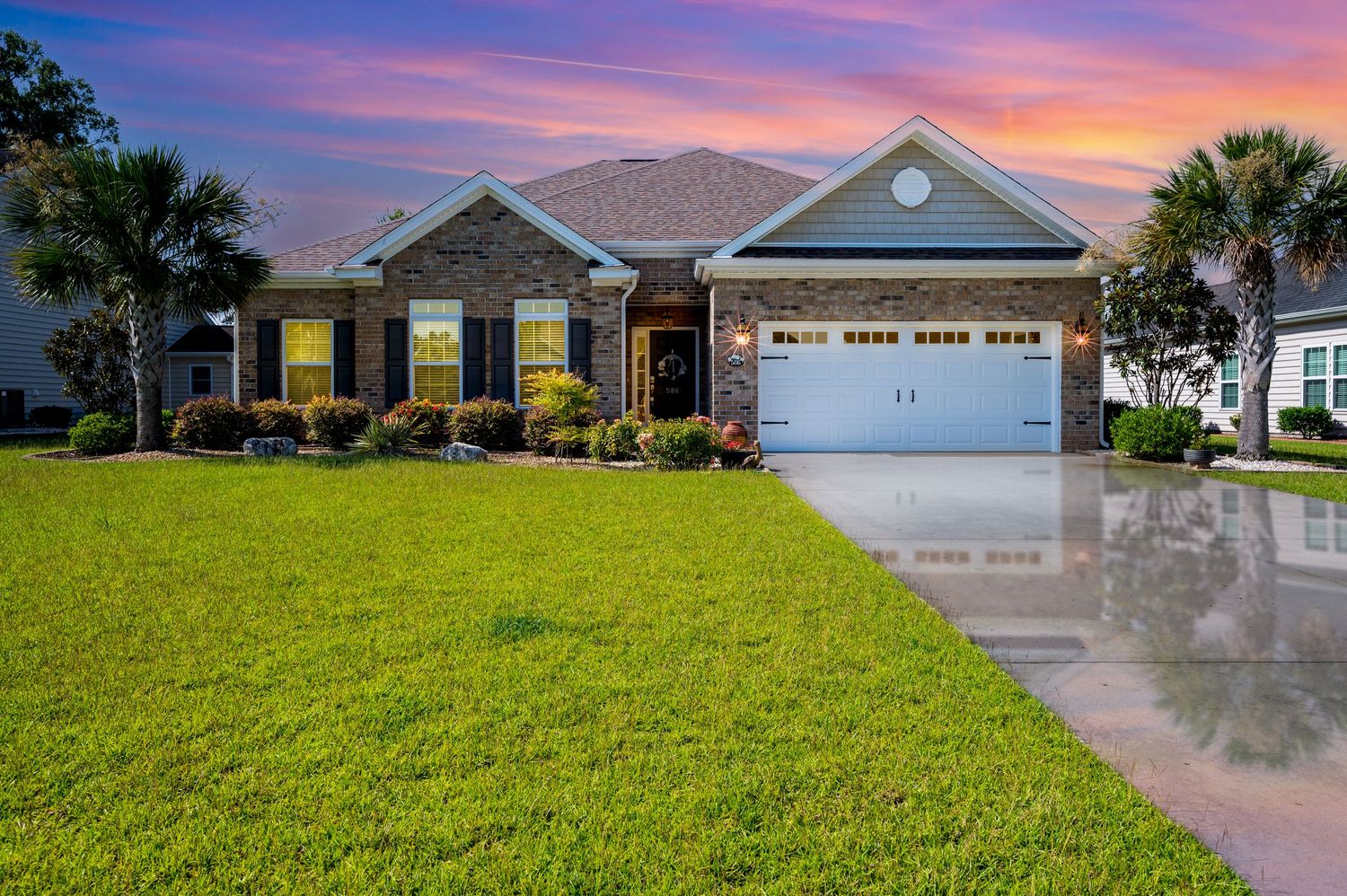 Brick ranch-style home with white garage door and manicured lawn at dusk.