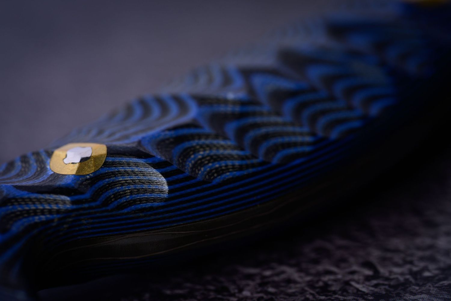 Extreme close-up of blue and black textured G10 knife handle scales with gold brass pin detail.
