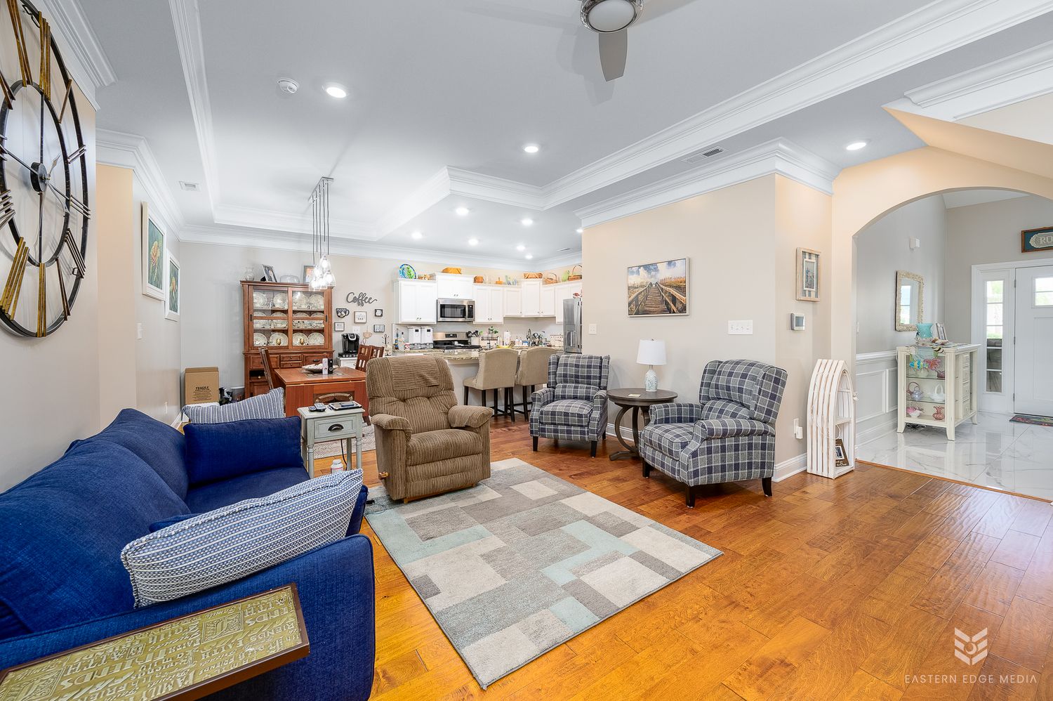 Bright open-concept living room with blue sofa, hardwood floors, and view into kitchen with stainless appliances.