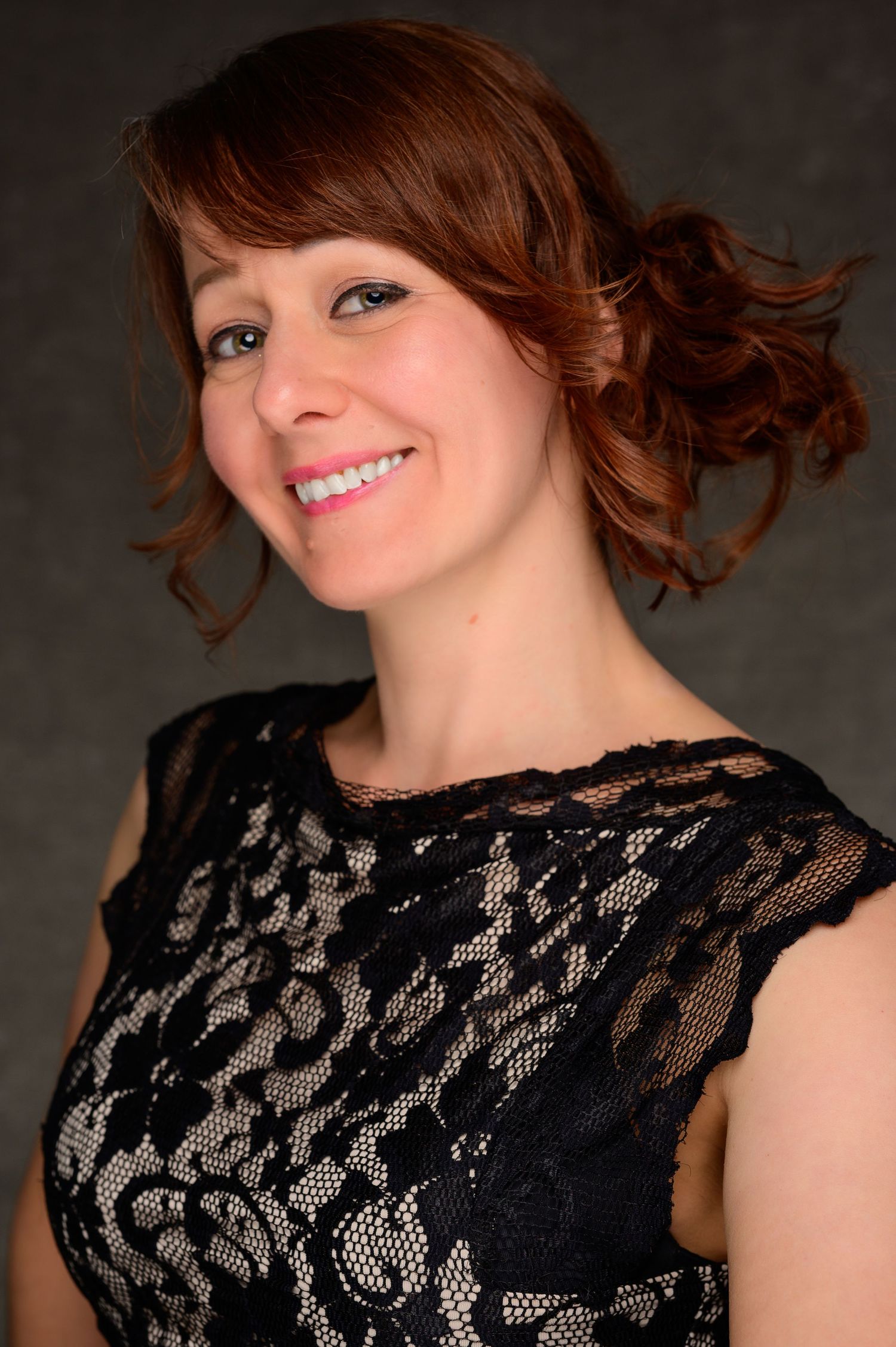 Smiling redhead woman with updo hairstyle wearing black lace dress in studio portrait.