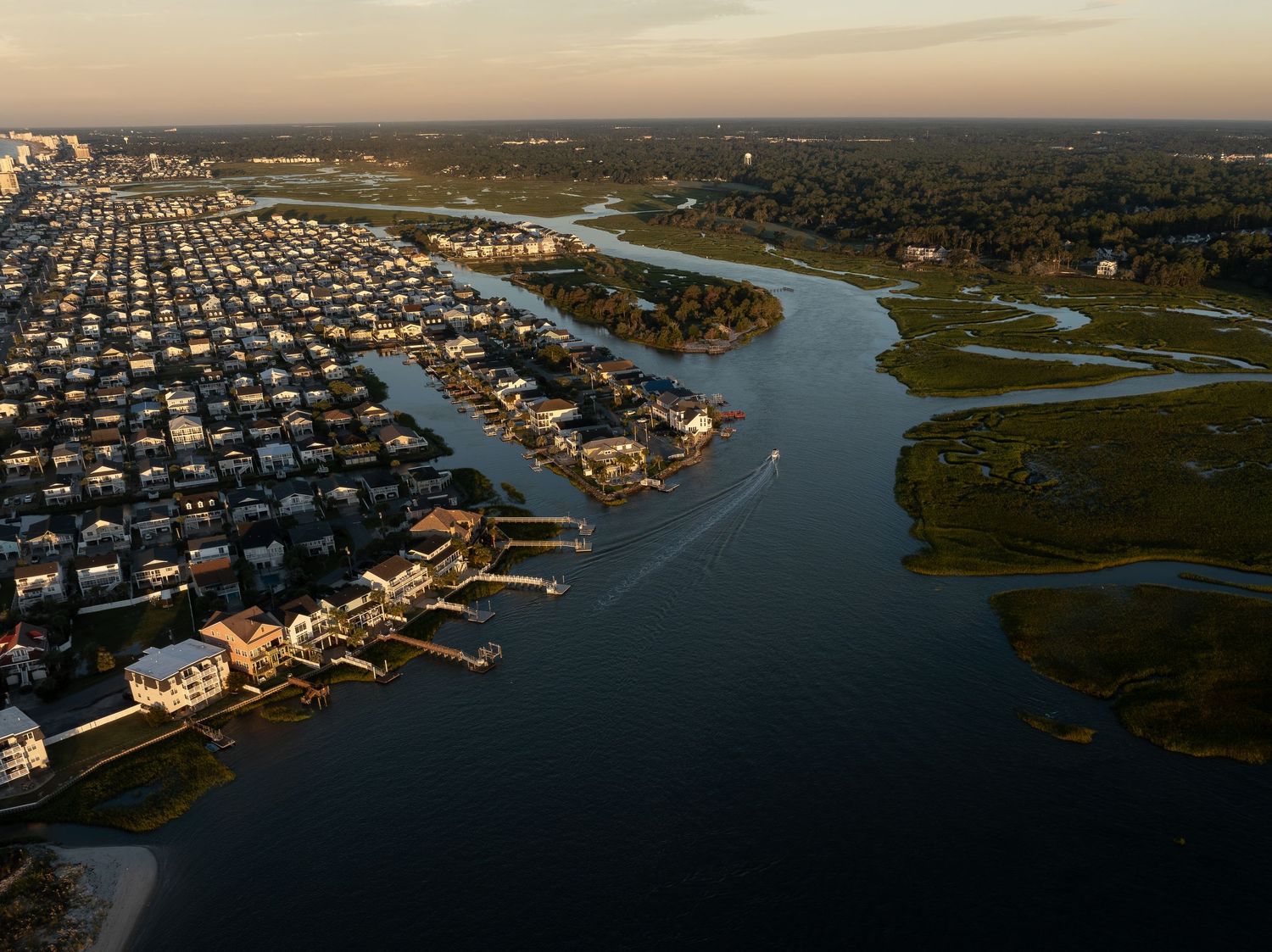 Aerial dusk view of a coastal community with waterfront homes, docks, winding waterways, and marshland.