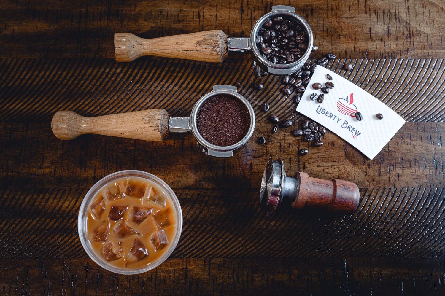 Espresso portafilter, coffee beans, and iced drink on dark wooden surface.