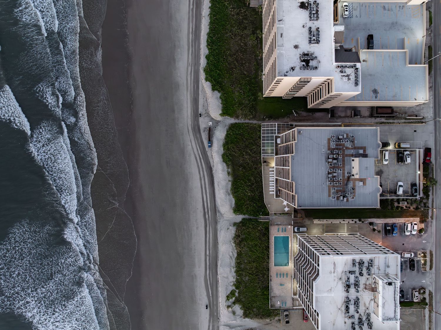 Aerial view of oceanfront homes with pool, sandy beach, and ocean waves along a coastal neighborhood.