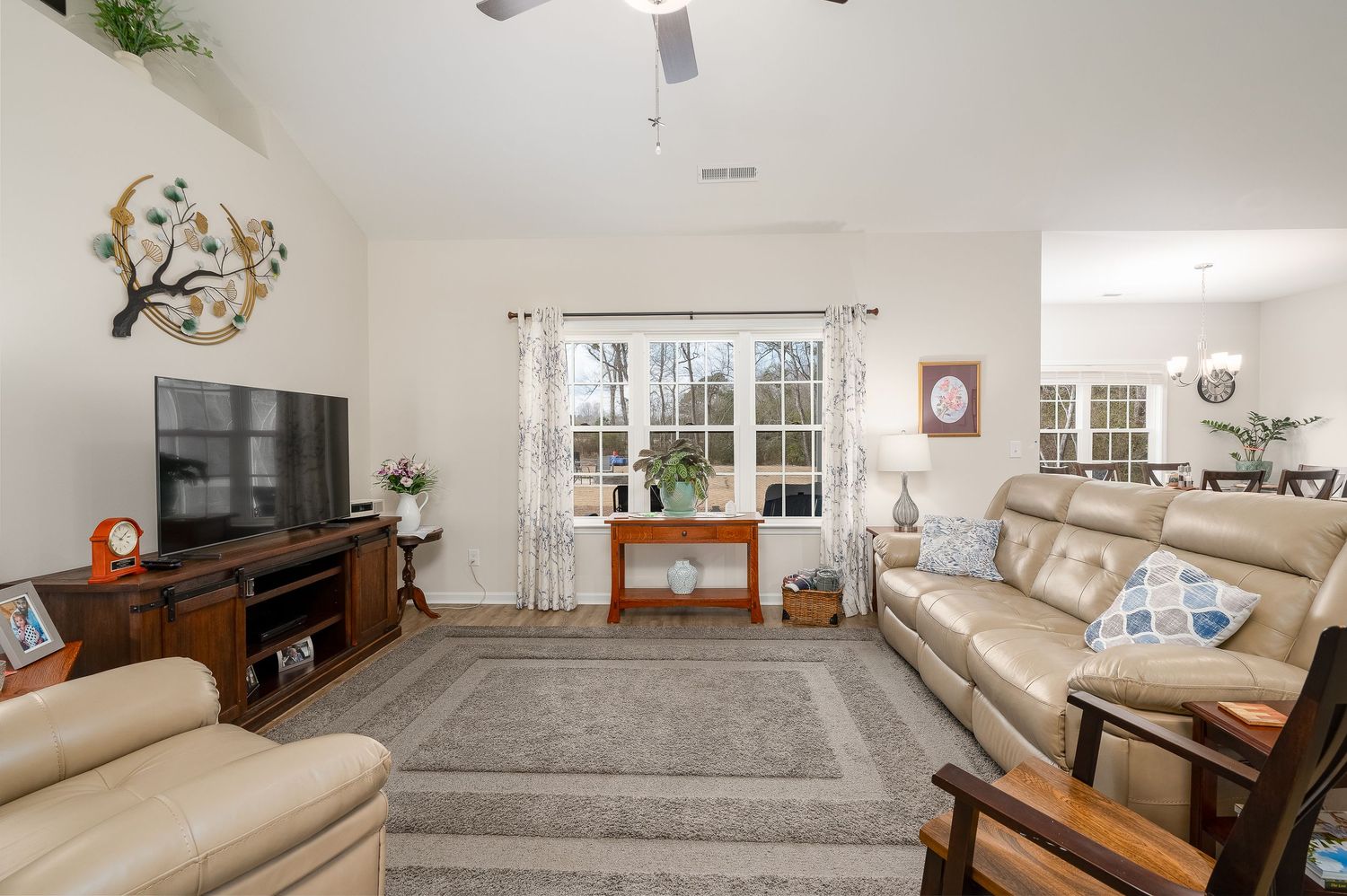 Comfortable living room with beige leather sofas, large TV, area rug, and bright windows.