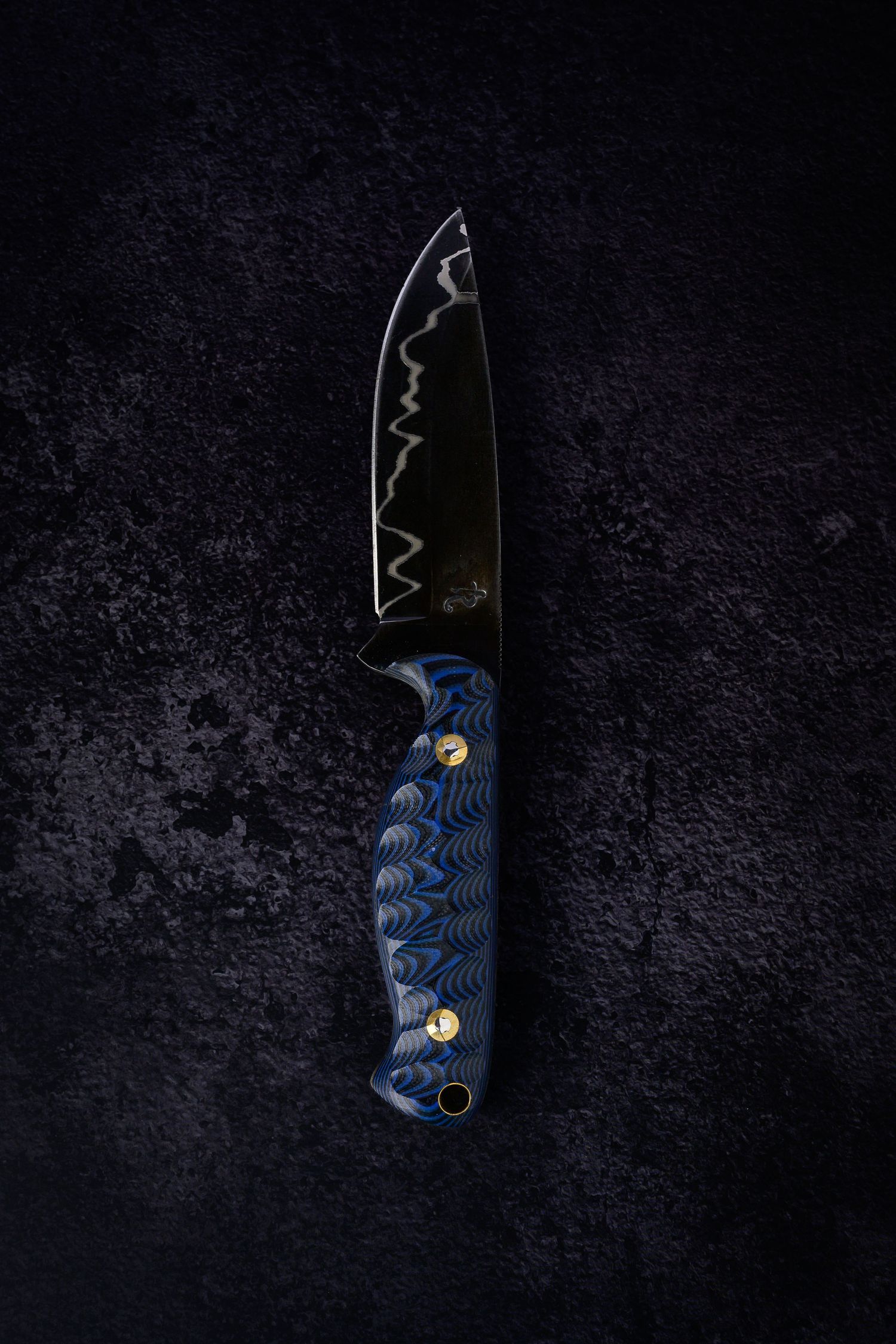Custom fixed blade knife with black Damascus steel blade and blue wave-patterned G10 handle on dark surface.