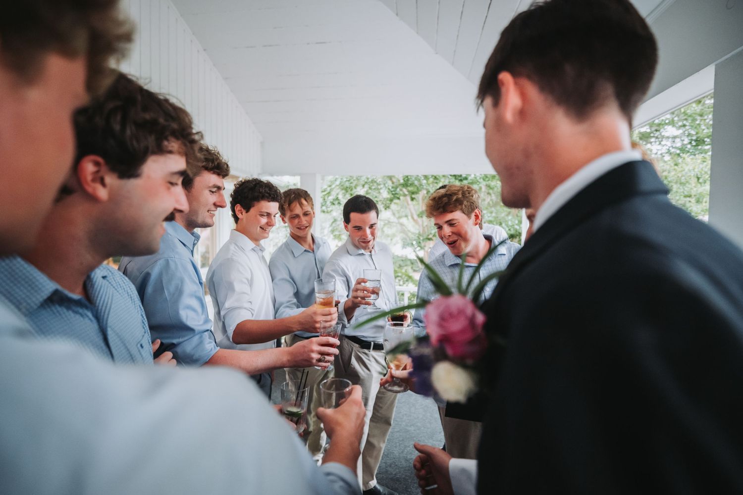 Groomsmen in light blue shirts gather around groom in black suit before wedding ceremony.