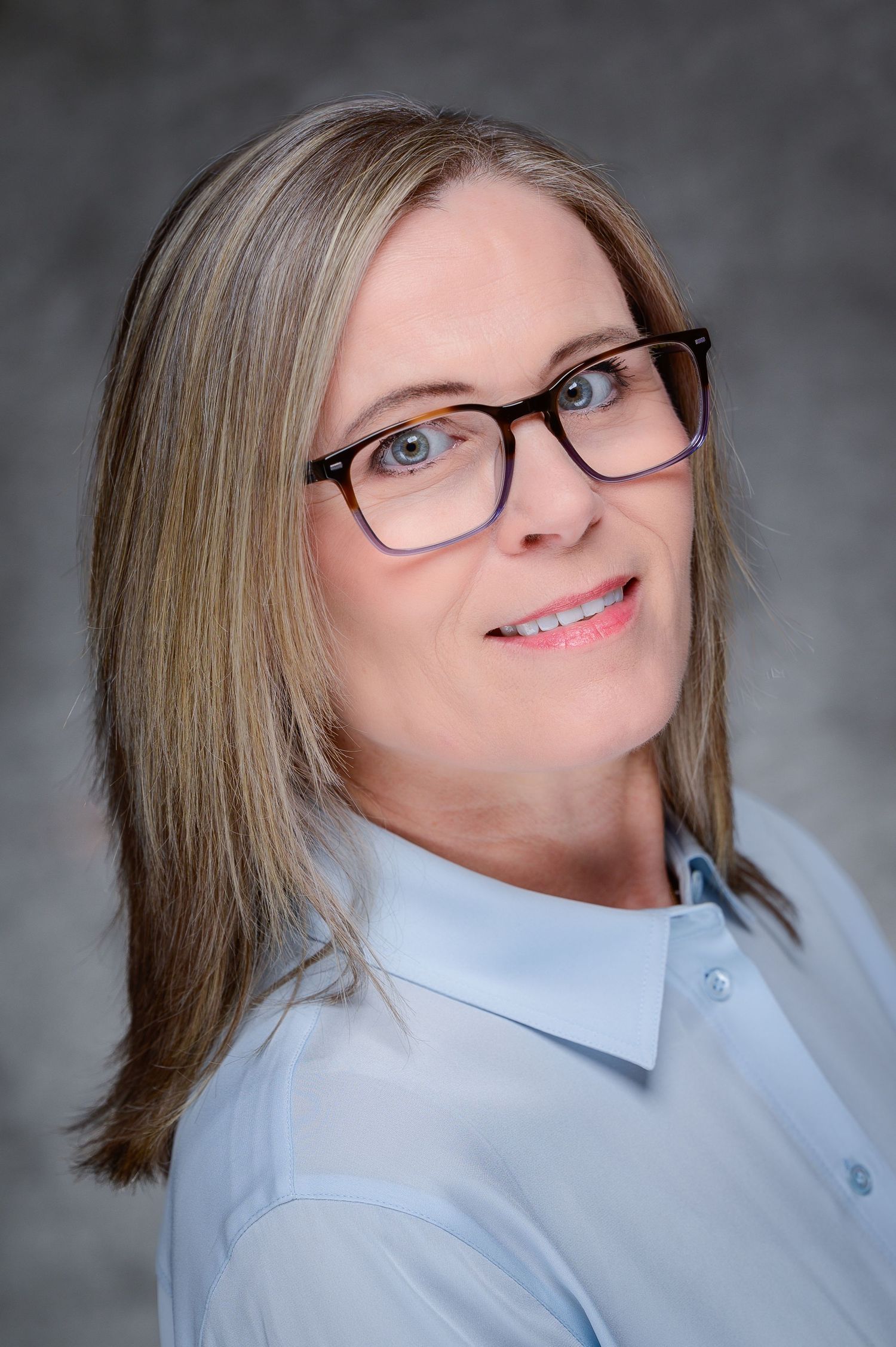 Smiling woman with glasses and blonde hair in professional headshot on gray background.