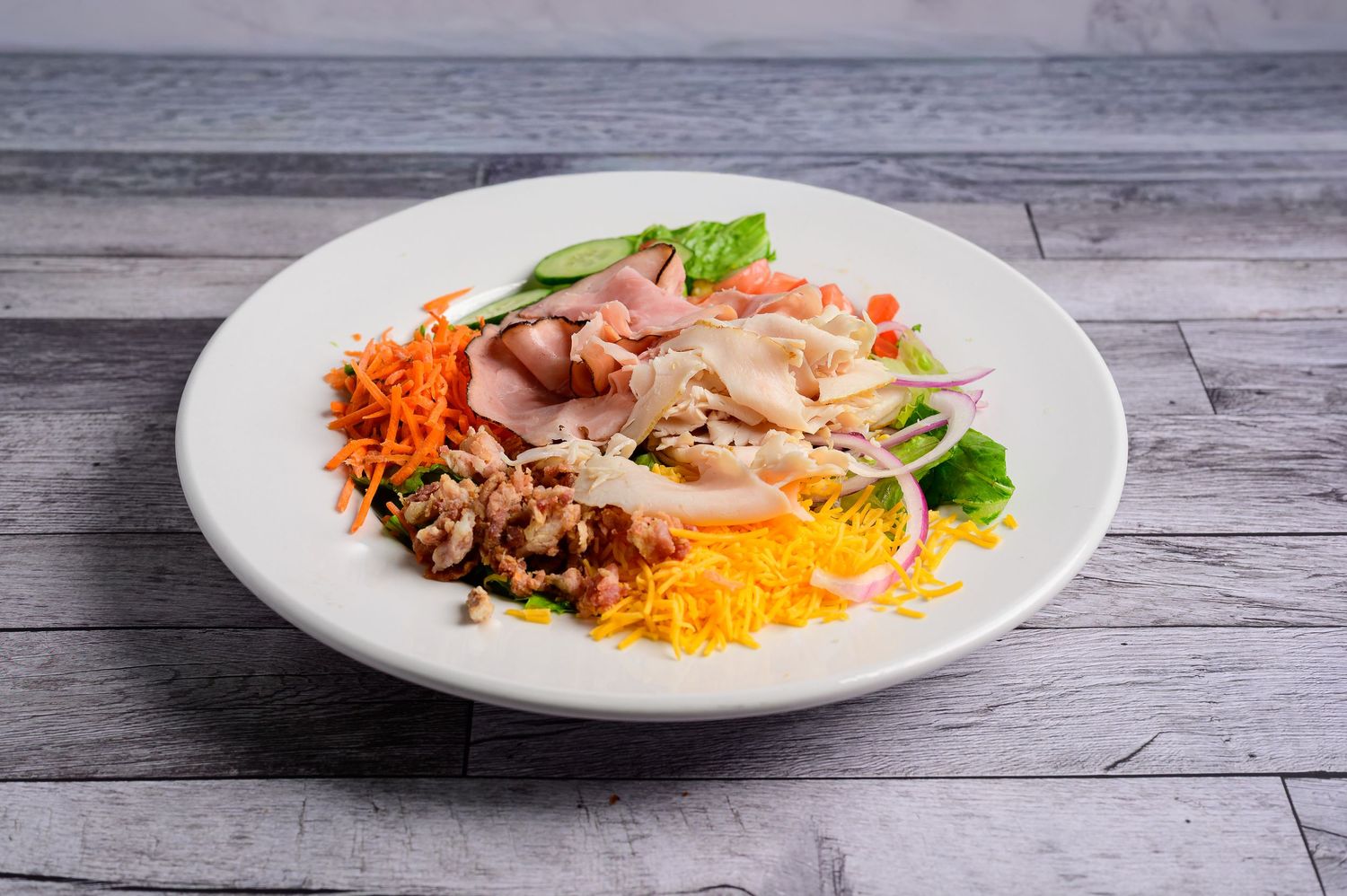 Fresh Cobb salad with chicken, carrots, cheese, bacon, and greens on a white plate.