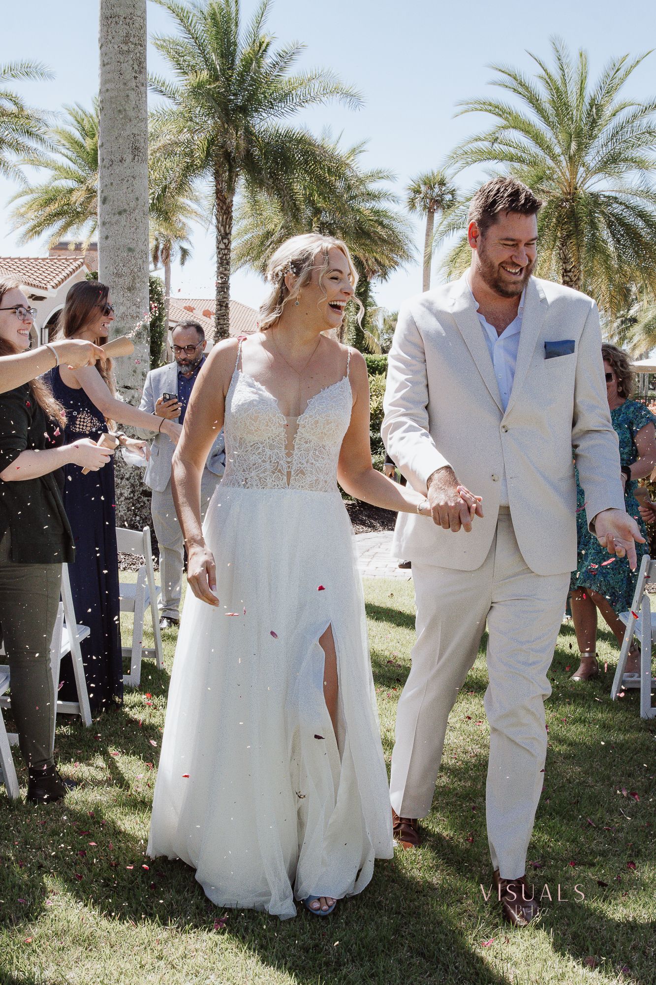 Wedding party celebrating and dancing outdoors under palm trees on a sunny day at a tropical venue.