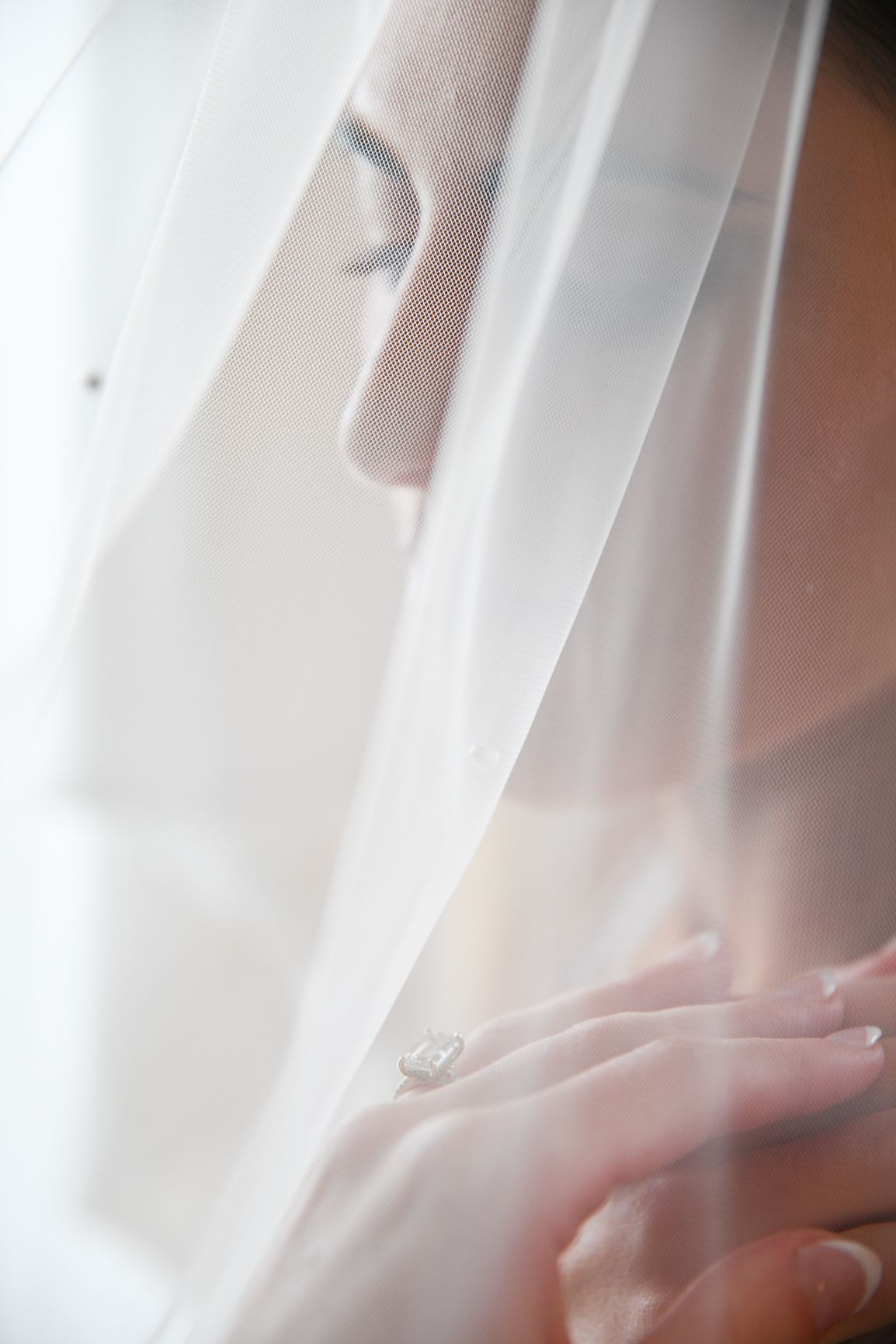 A delicate white veil softly drapes over a profile view, creating an ethereal bridal portrait with soft lighting.