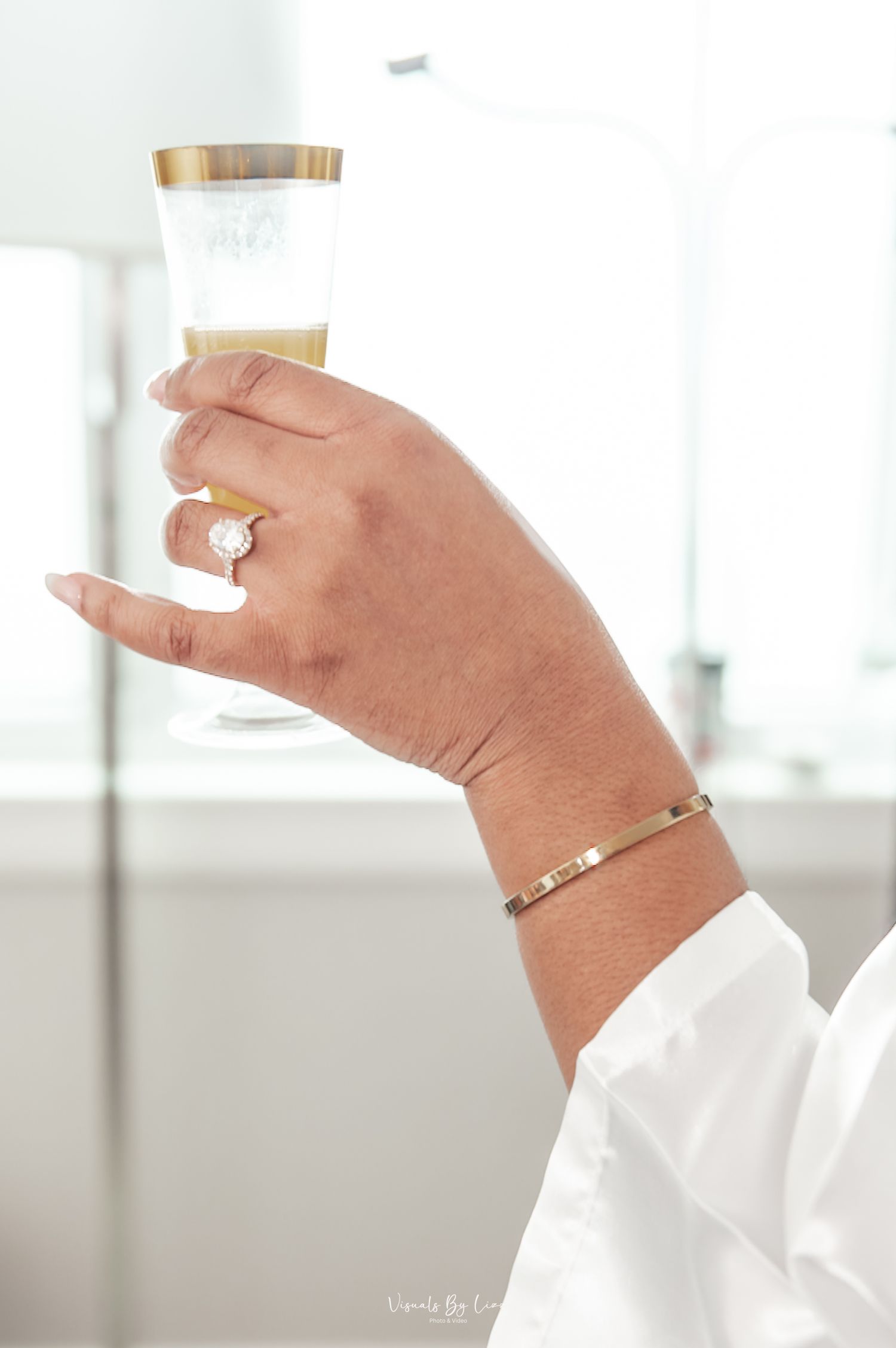 Close-up view of hands wearing elegant rings holding white ceramic teacups against a bright interior background.