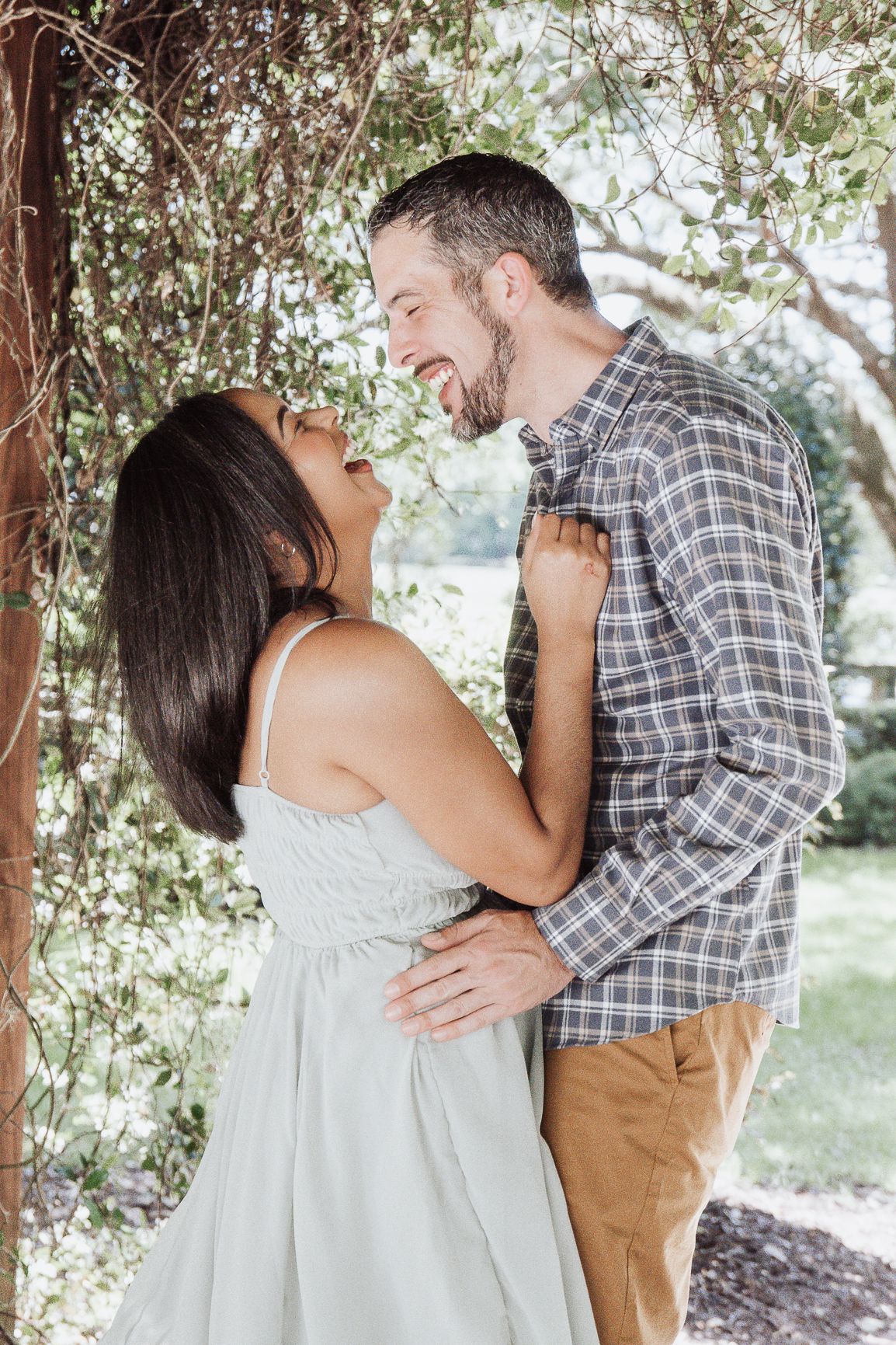 Romantic couple laughing together under tree branches in outdoor setting.