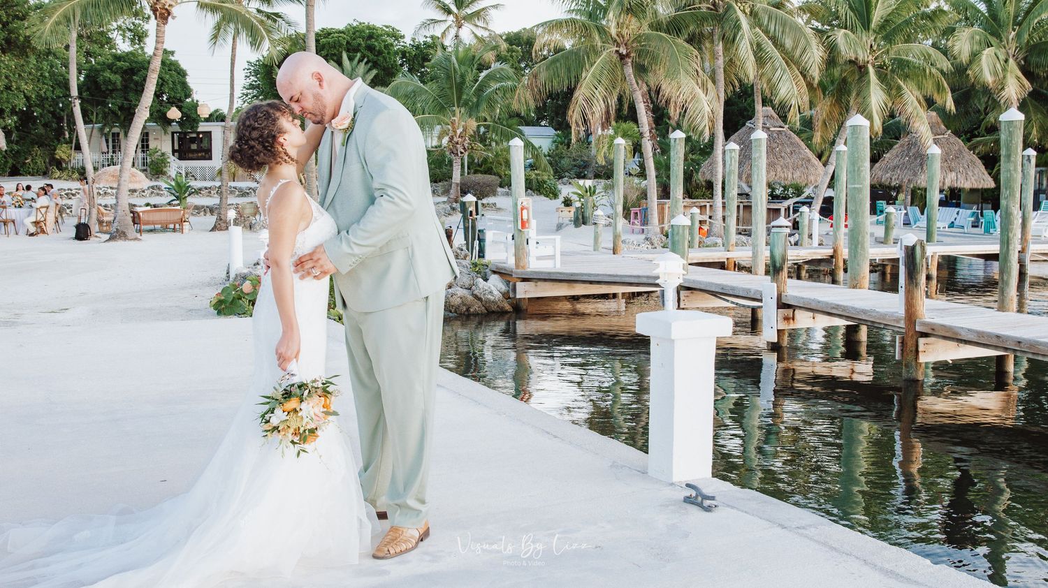 Newlyweds walk along a tropical marina boardwalk surrounded by palm trees and boats on a sunny day. Islamorada, Florida