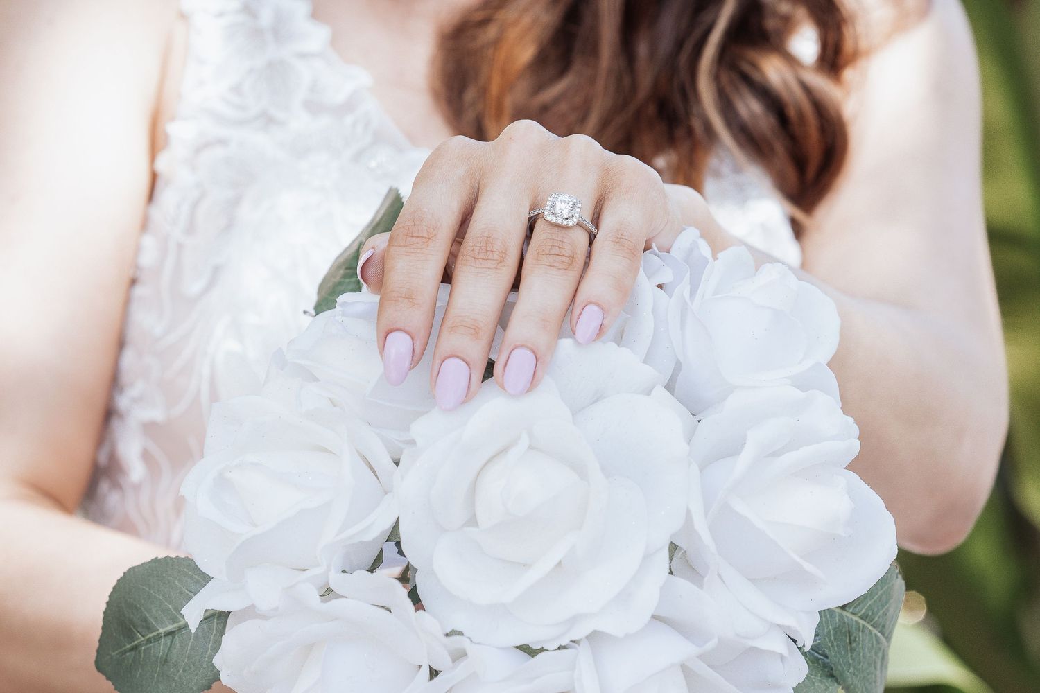 Bridal manicure detail with engagement ring and white rose bouquet.