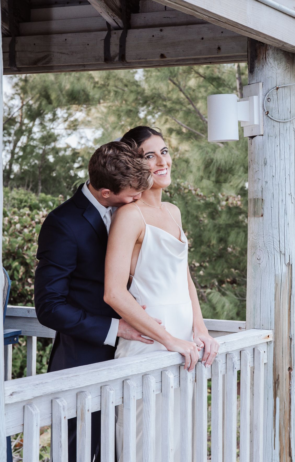 Romantic couple embraces on a white wooden porch with multiple reflections in mirrors creating a dreamy effect.