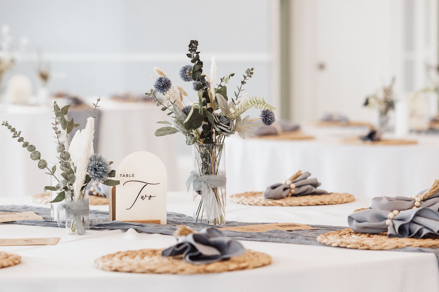 Elegant table settings with woven placemats, delicate floral centerpieces, and soft natural light in a minimalist dining space.