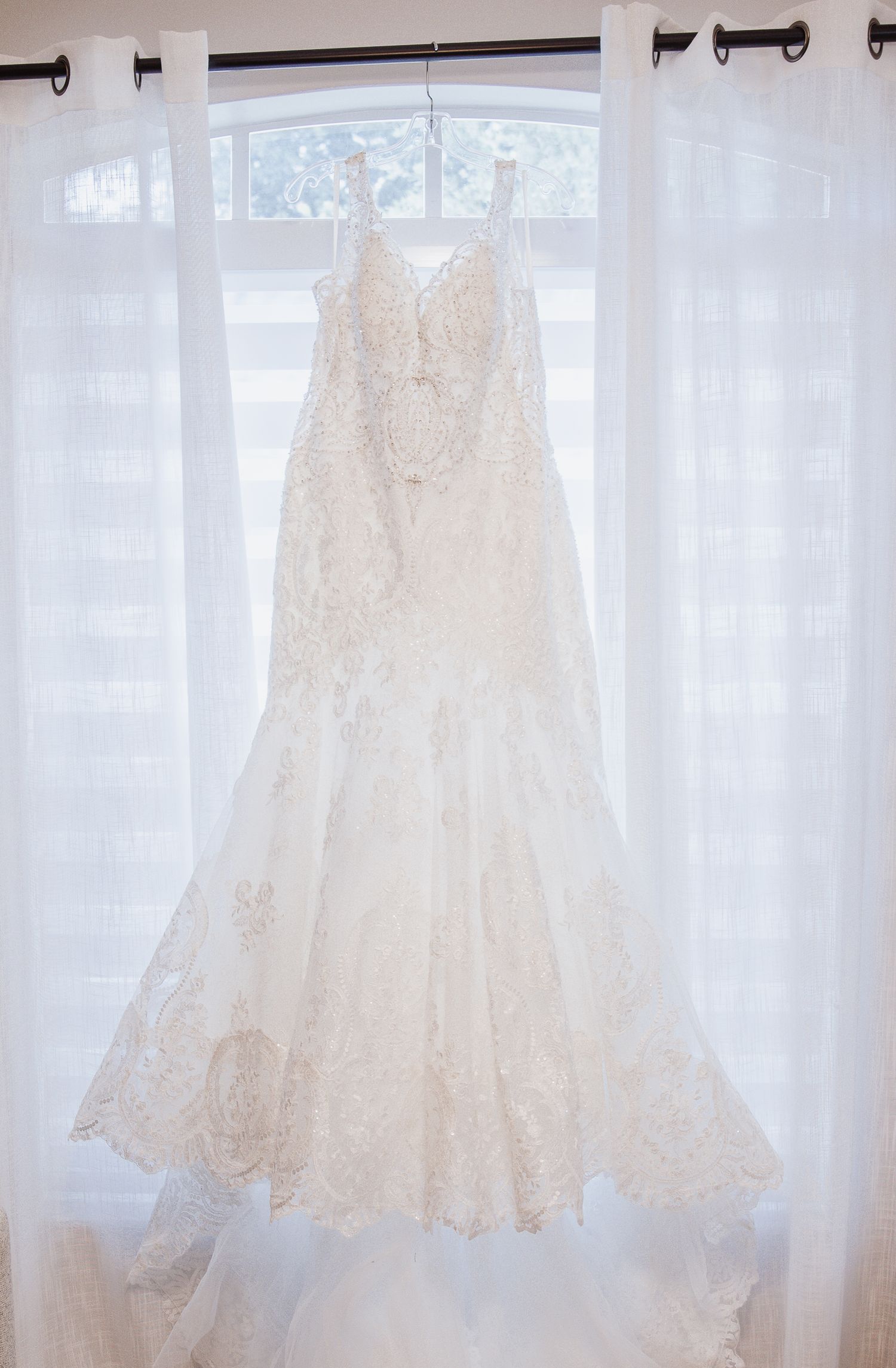 Multiple white wedding dresses hanging on display against sheer curtains.