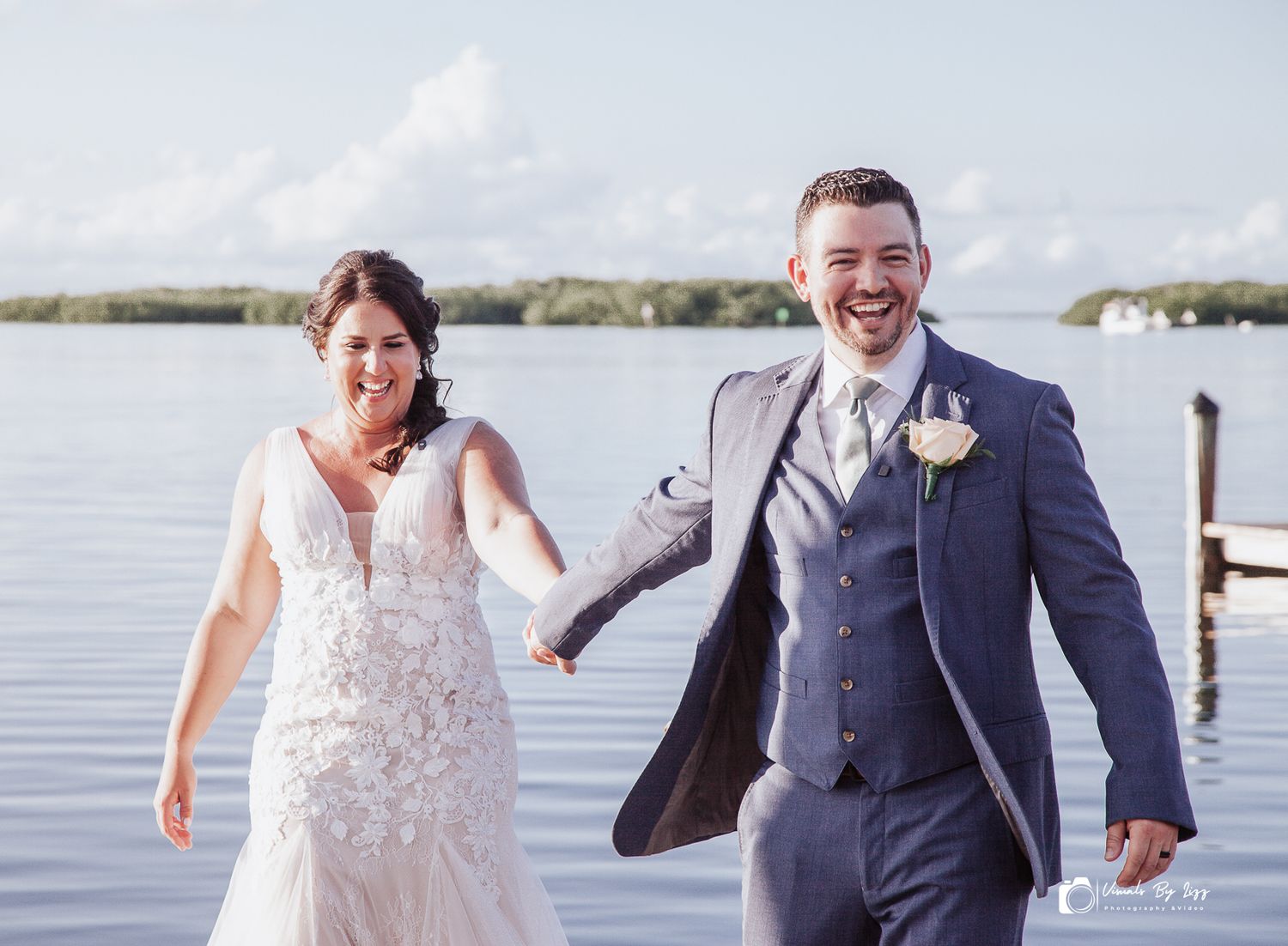 A couple in wedding attire holds hands and laughs joyfully while walking along a waterfront dock. Islamorada, Florida
