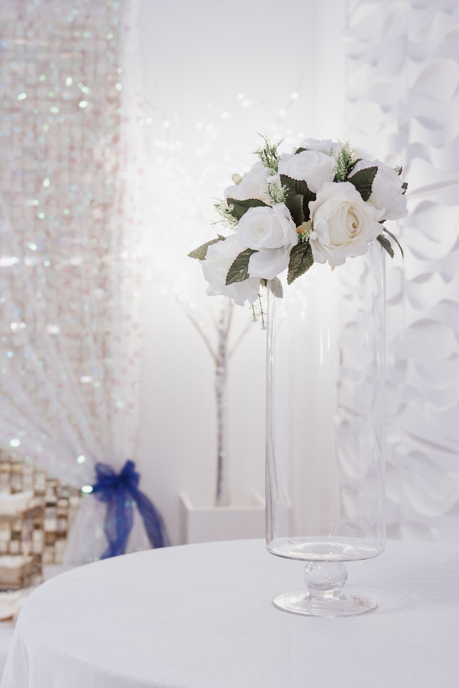 White roses and lilies arranged in a tall glass vase with crystal decor elements in an elegant wedding setting.