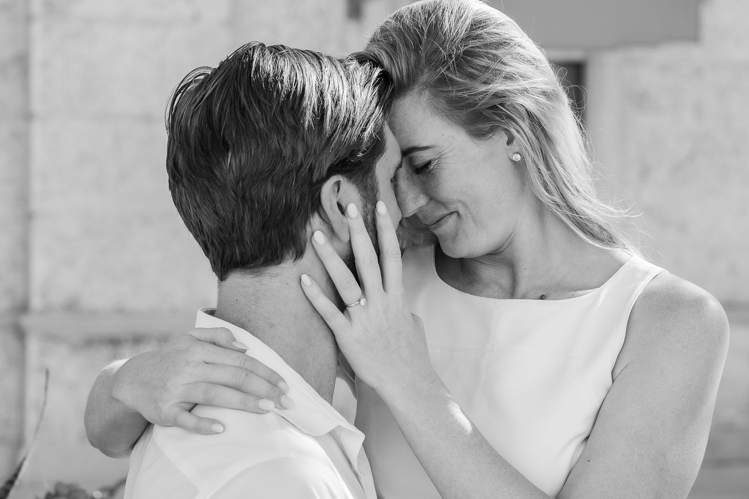 Black and white photo of a romantic couple sharing an intimate moment, woman smiling and touching man's face.
