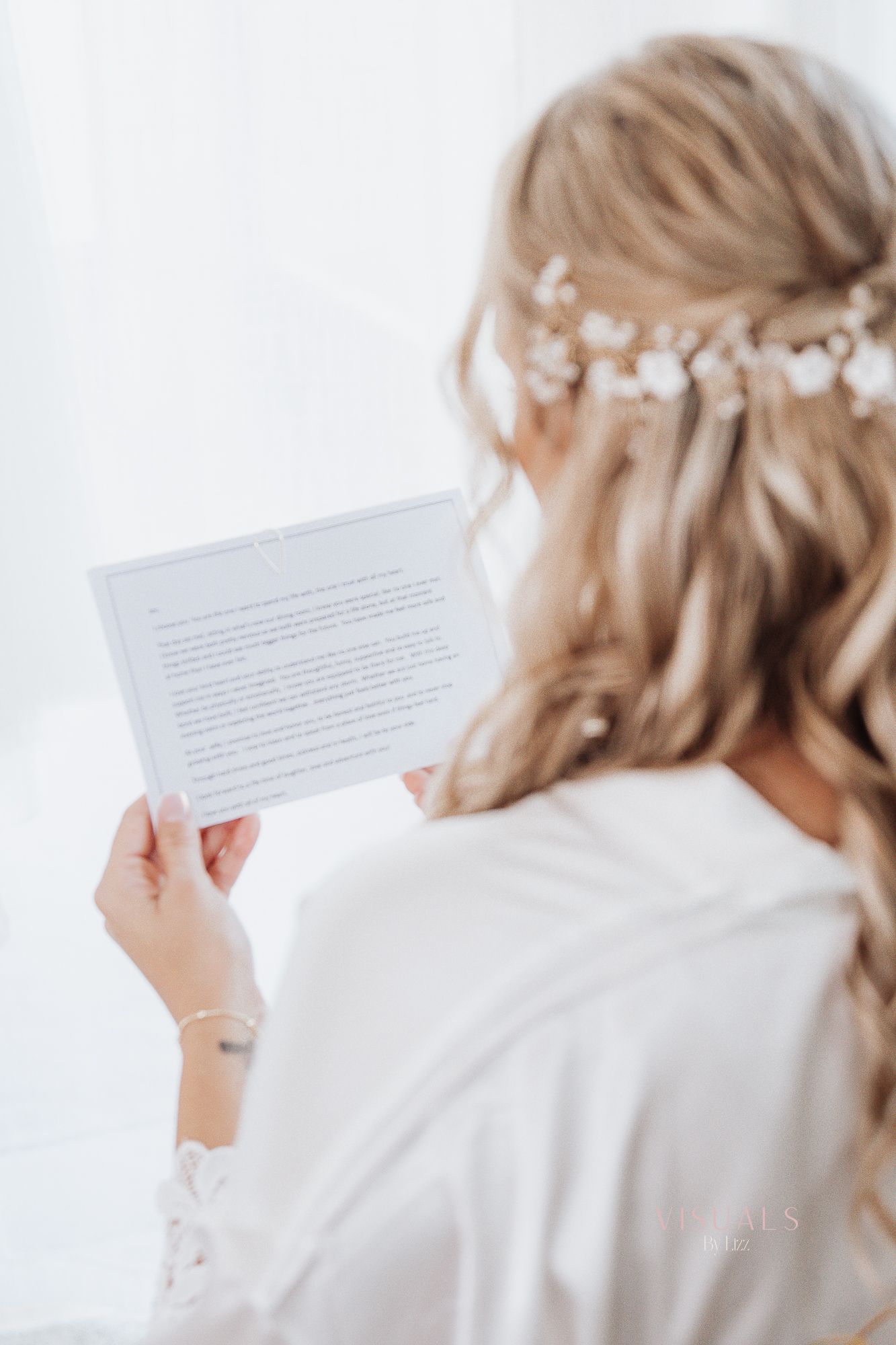 Bride in white robe reading a letter during wedding morning preparations.