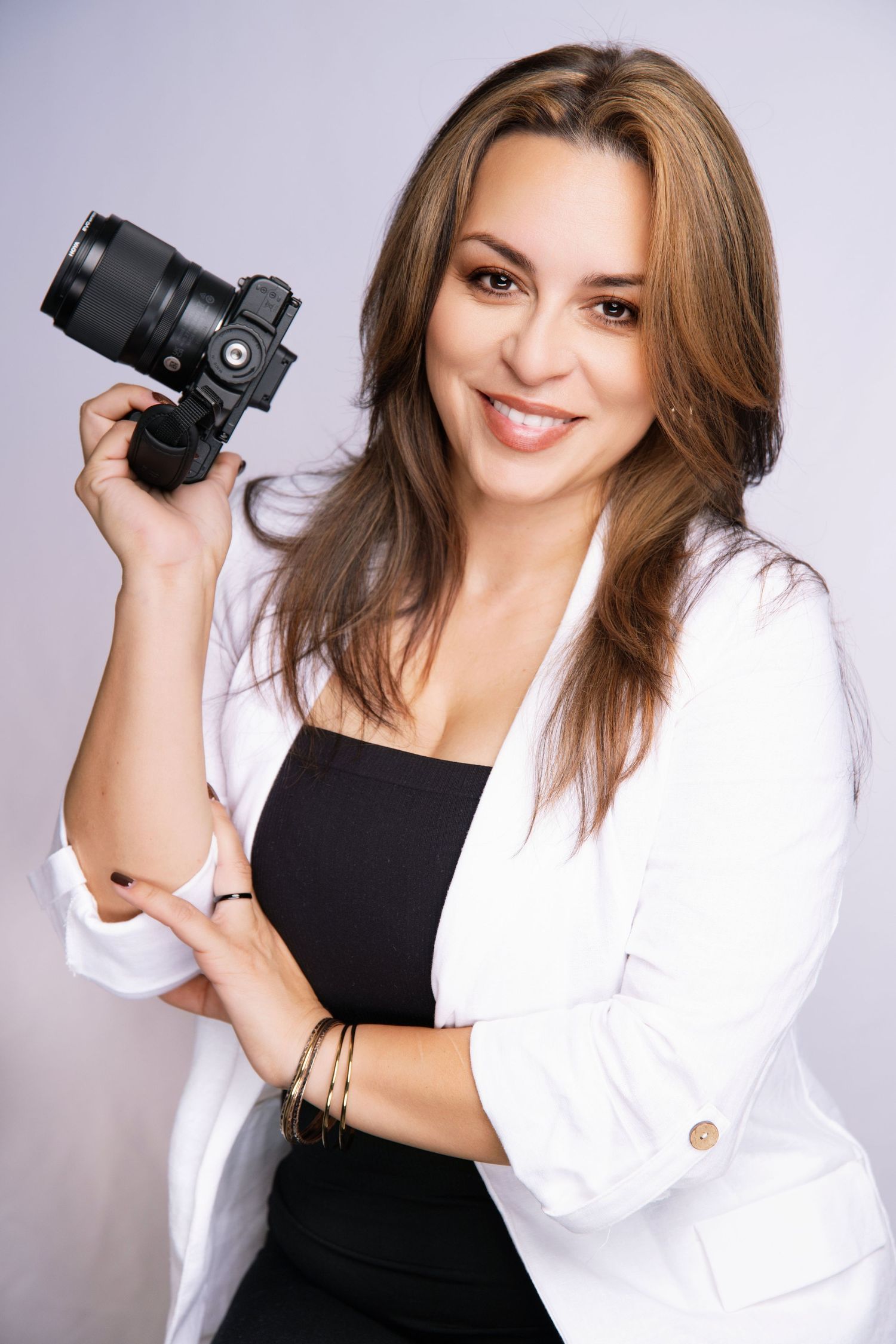 Professional photographer wearing white blazer and black top while holding DSLR camera.